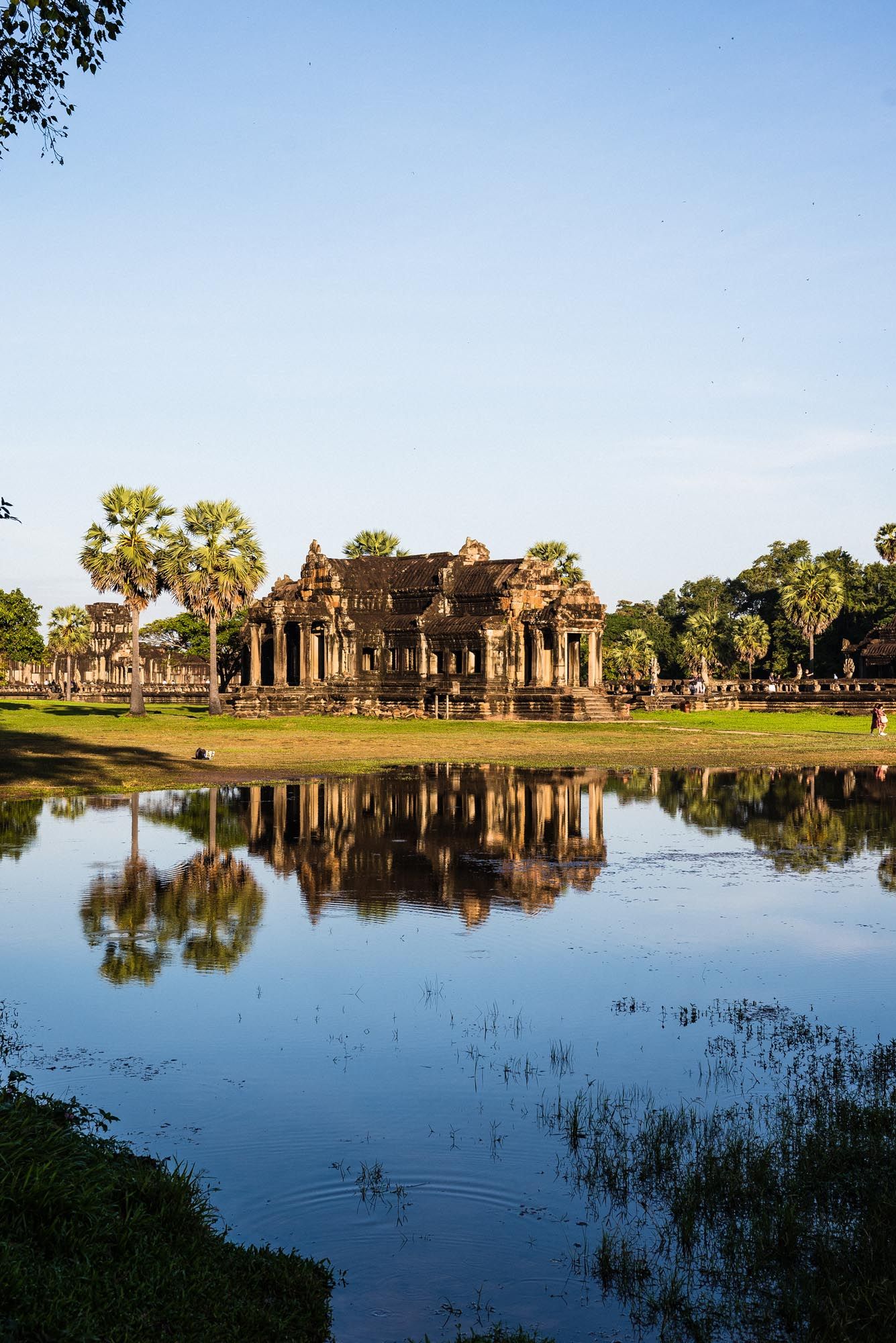 Ancient temple ruins of Angkor Wat reflect in calm waters of surrounding moat during golden sunset in Cambodia.