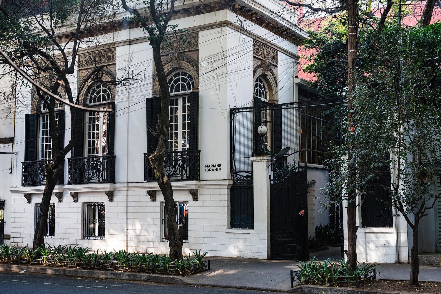 White neoclassical building exterior with tall arched windows and stone columns in an urban setting.