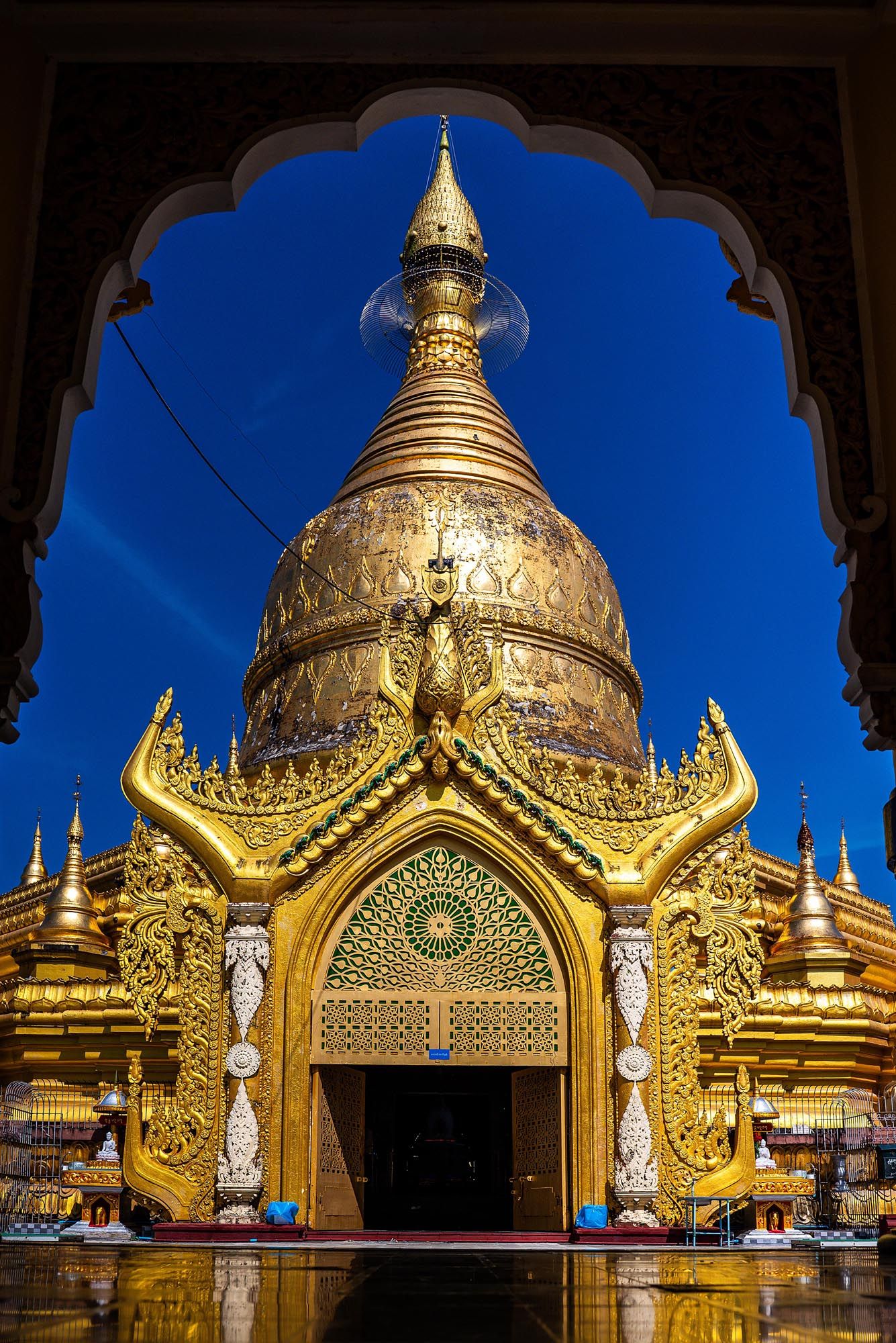 Golden spires and domes of a Buddhist temple shine brilliantly against a deep blue evening sky in Myanmar.