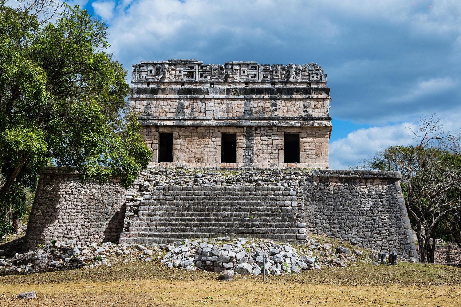 Ancient Mayan stone temple ruins with detailed architectural features stand against a blue sky in Yucatan, Mexico.