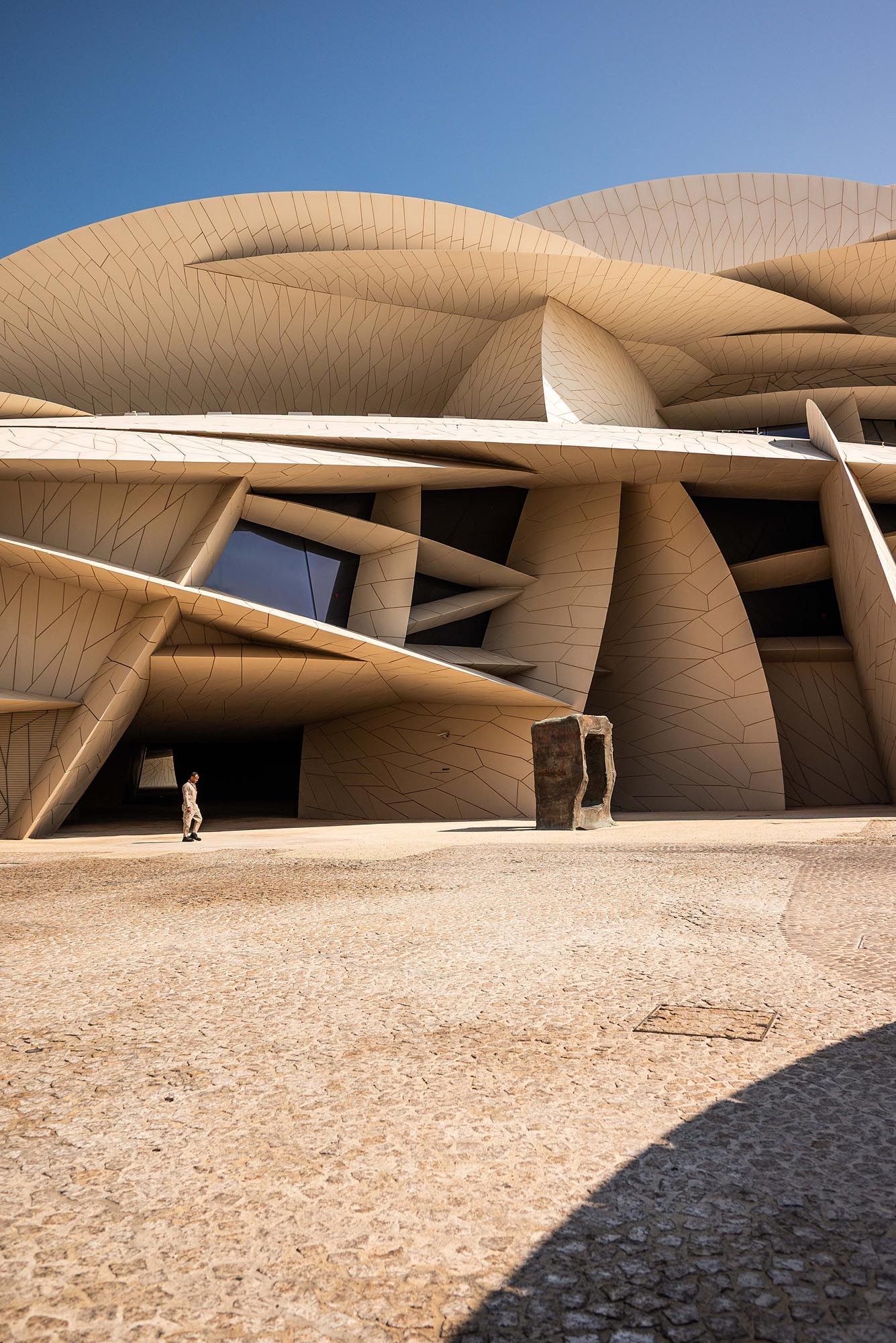 Modern architectural facade of the National Museum of Qatar featuring curved beige walls and angular geometric design elements.