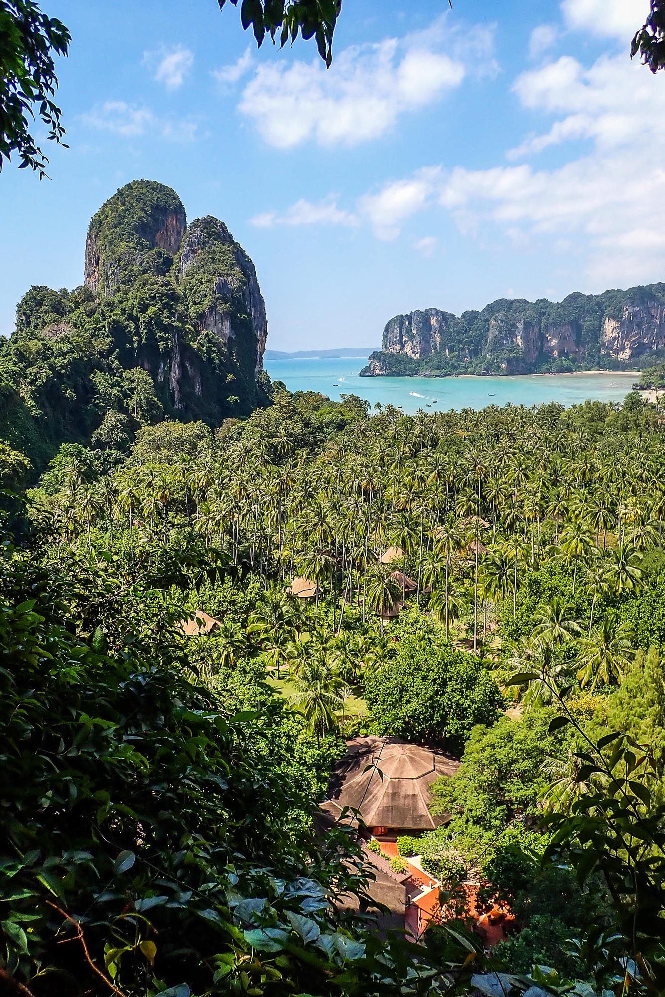 Scenic view of limestone cliffs and turquoise waters at Railay Beach in Thailand with lush jungle and bungalows below.