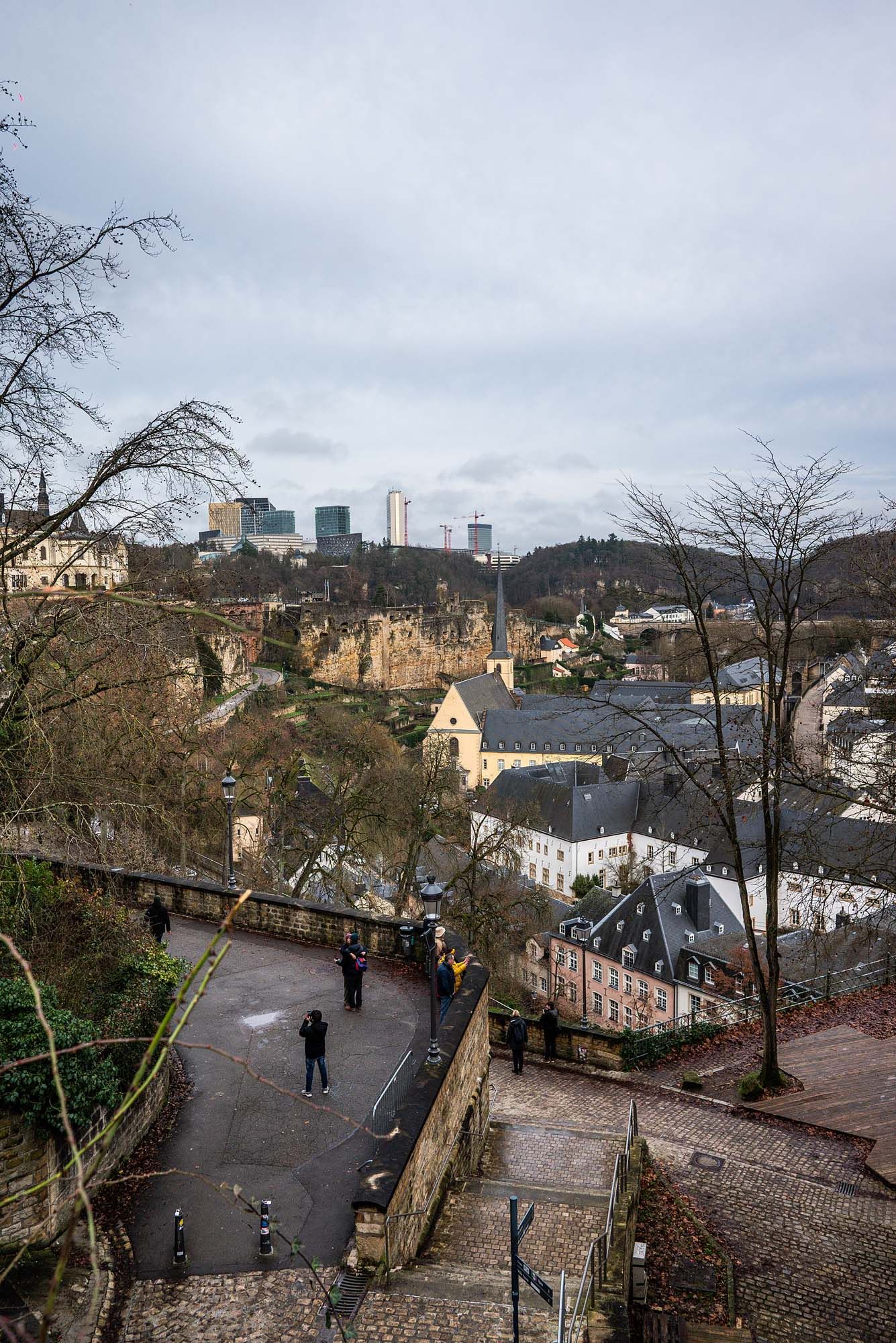 Panoramic view of Luxembourg City's historic district with winding paths and stone walls under cloudy skies.