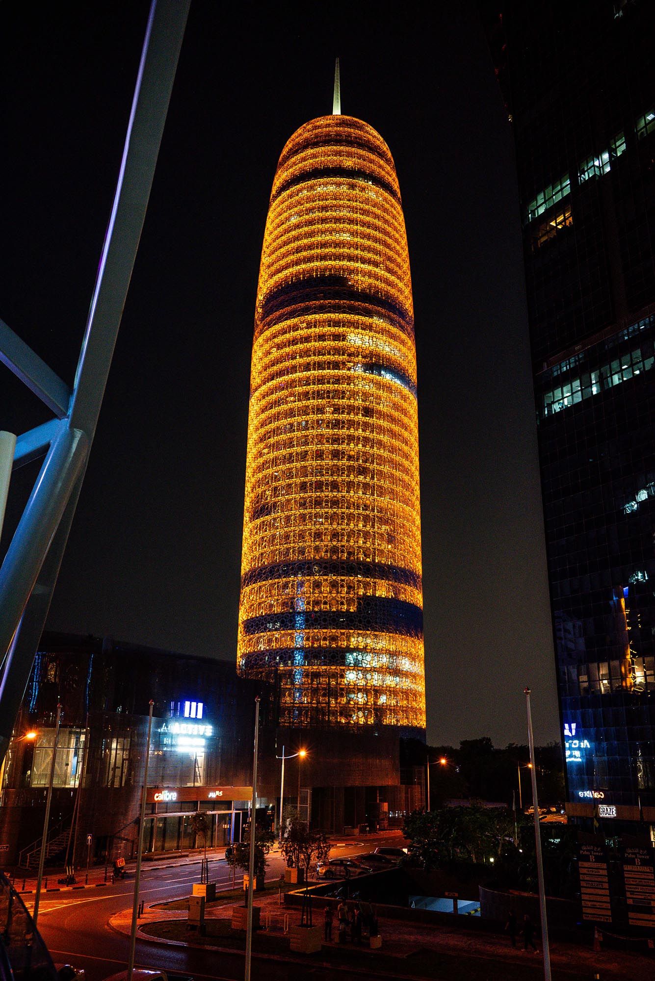 Illuminated orange cylindrical building glowing at night with multiple architectural levels in an urban setting.