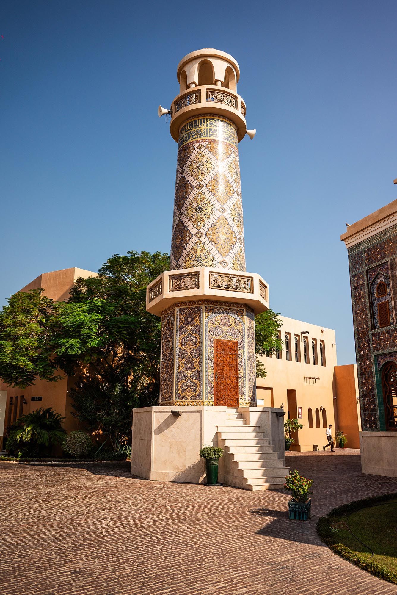 Ornate Islamic minaret with intricate geometric patterns and mosaic designs stands against blue sky in traditional architecture.