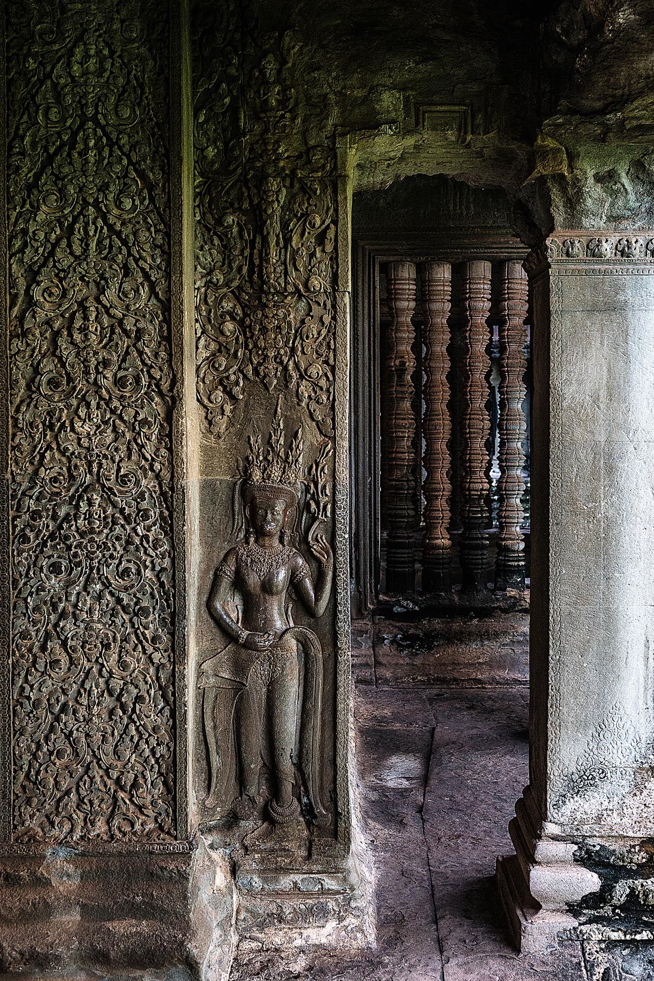 Ancient stone carvings and ornate wall decorations line a dark corridor in the historic Angkor Wat temple complex.