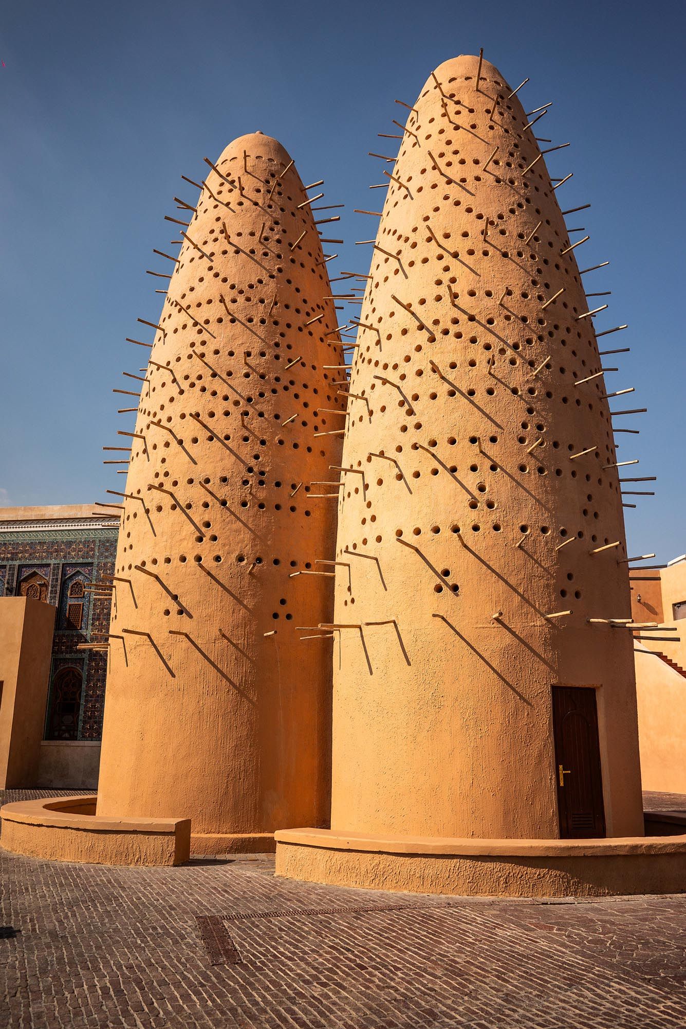 Traditional pigeon towers with spiked architectural details rise against blue sky at Dolatabad Garden in Isfahan, Iran.