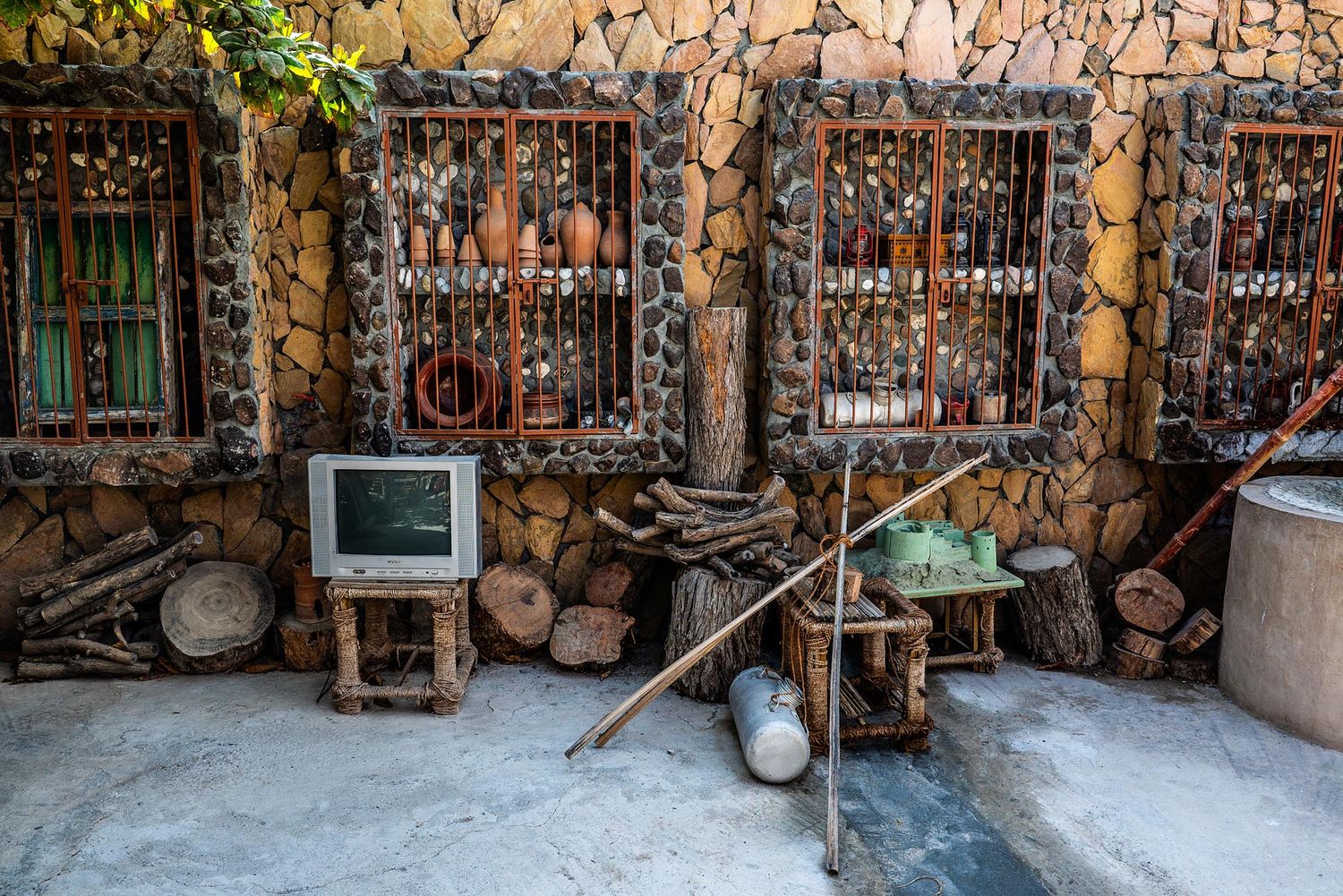 A rustic stone wall with vintage tools, farming equipment, and antique implements displayed in an outdoor museum setting.