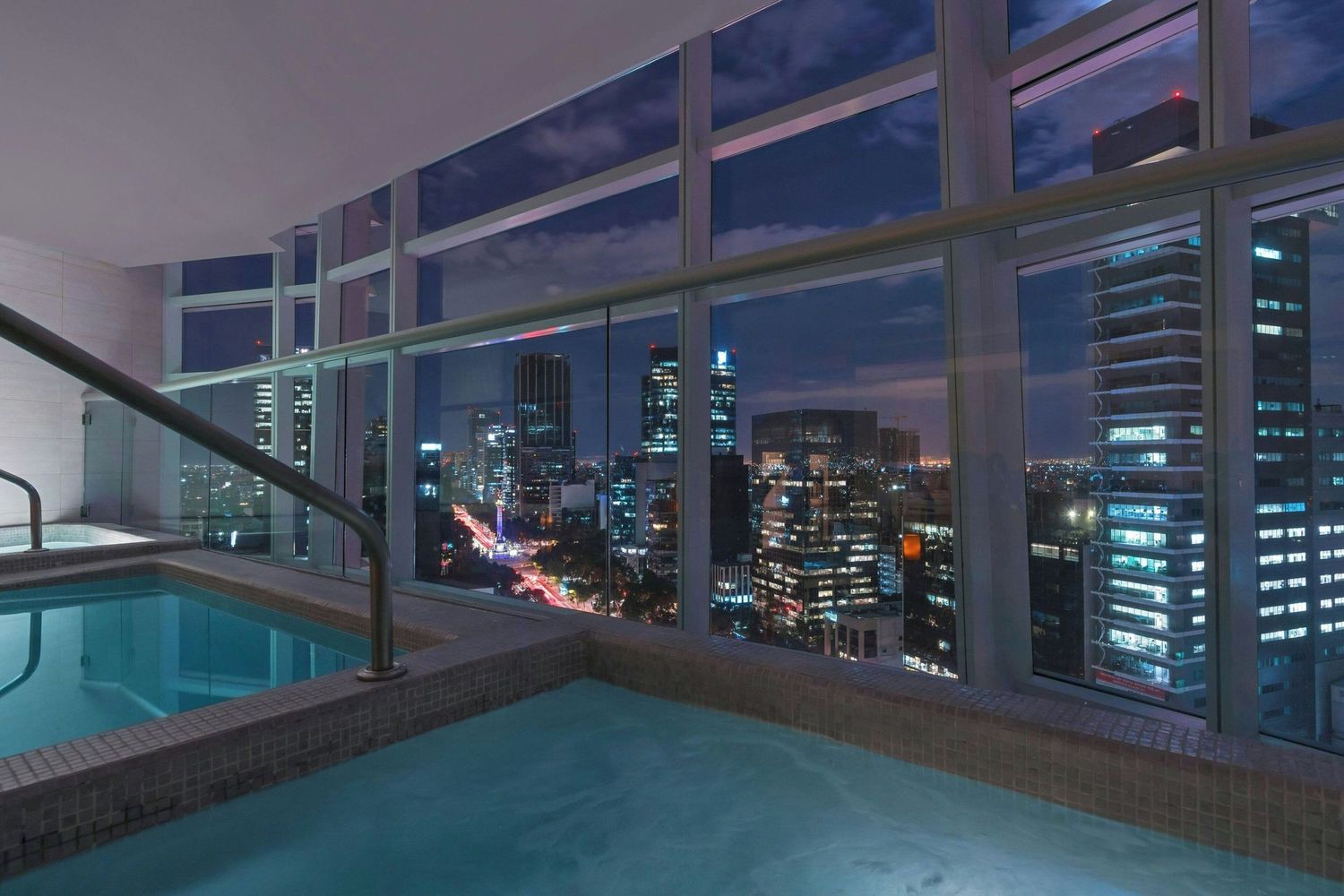 Panoramic view of a modern high-rise balcony overlooking a glowing city skyline at night.