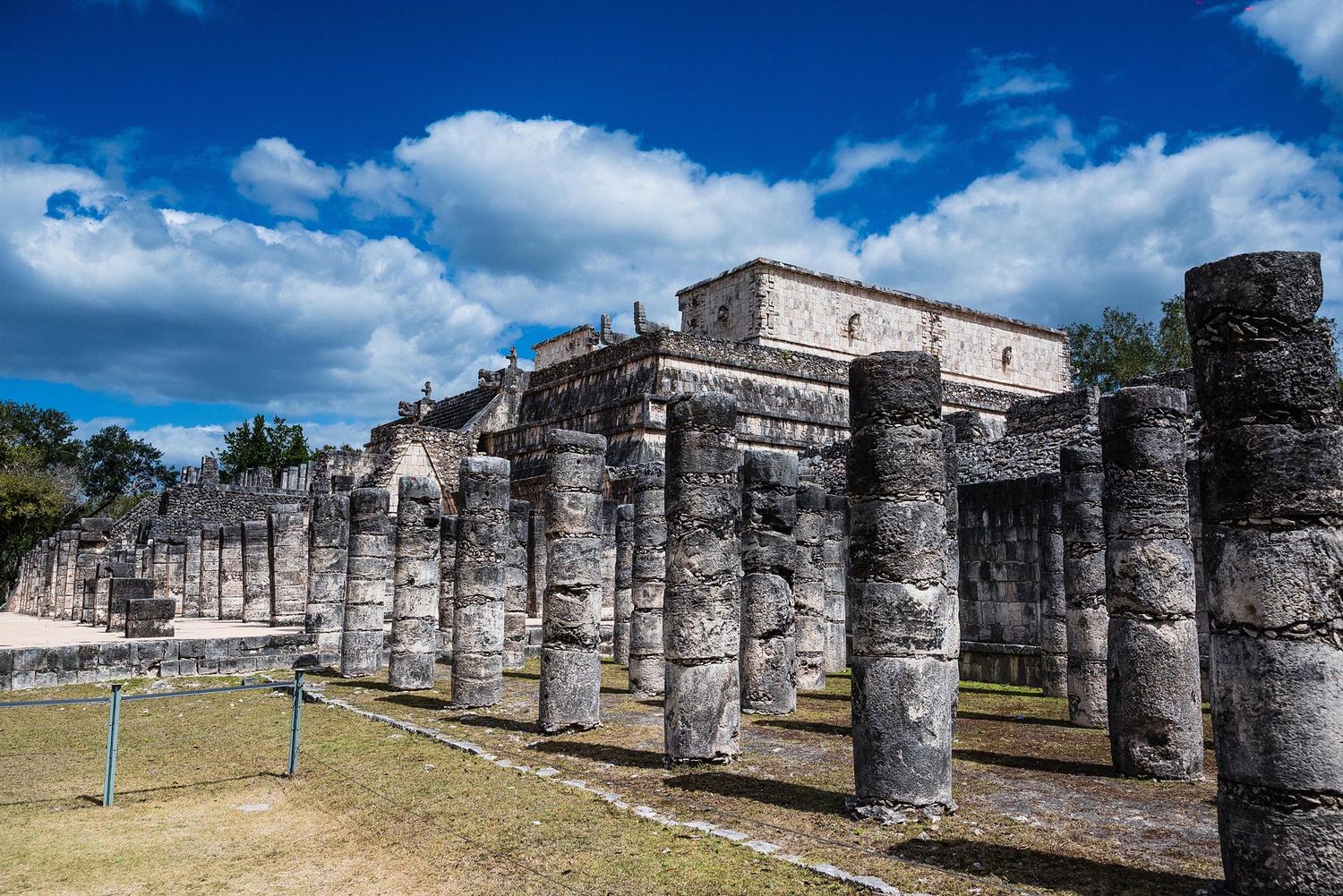Ancient stone columns stand against a bright blue sky at the Temple of a Thousand Warriors in Chichen Itza, Mexico.