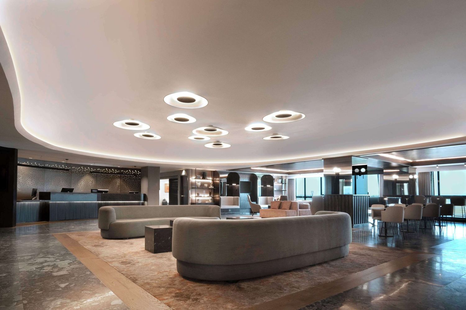 Modern office lobby with circular ceiling lights, curved concrete seating, and polished floors in a contemporary design.