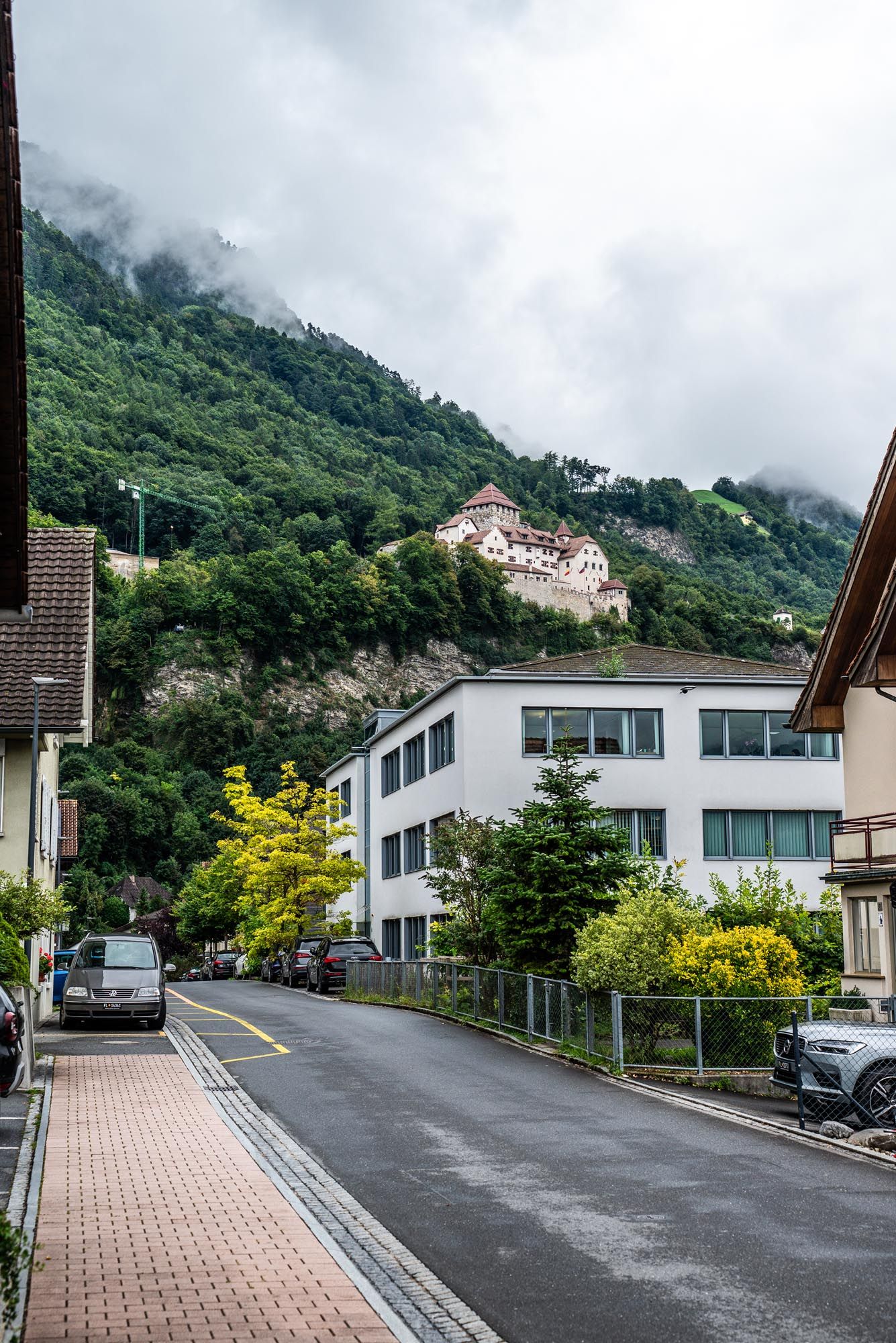 A steep residential street with modern houses and mountain views in Liechtenstein on a cloudy day.