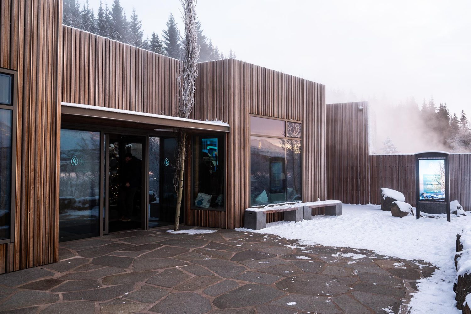A panoramic view of a modern wooden-clad building exterior with snow-covered landscape in winter.