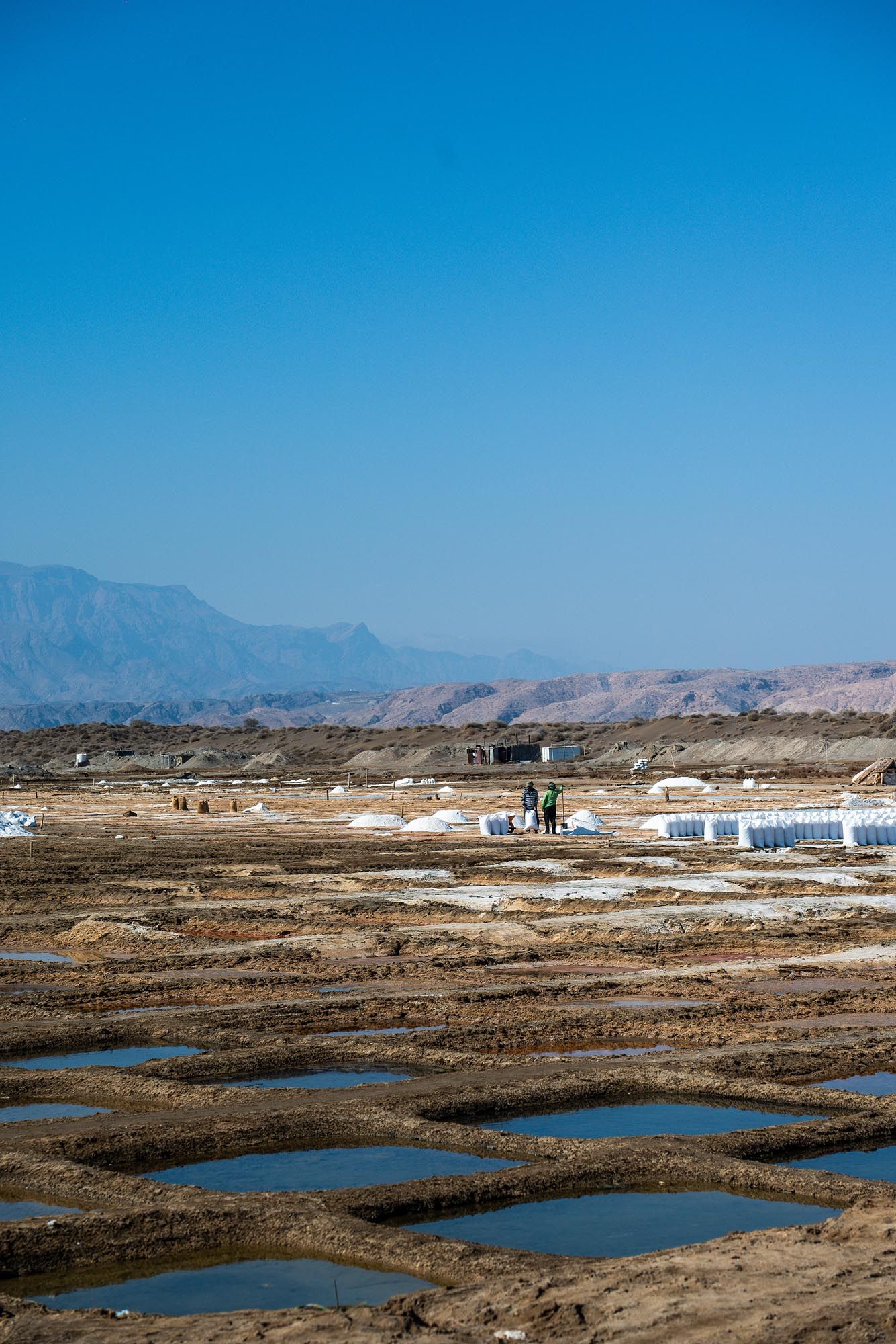 Panoramic view of salt ponds and mountains in a coastal landscape under bright blue sky.