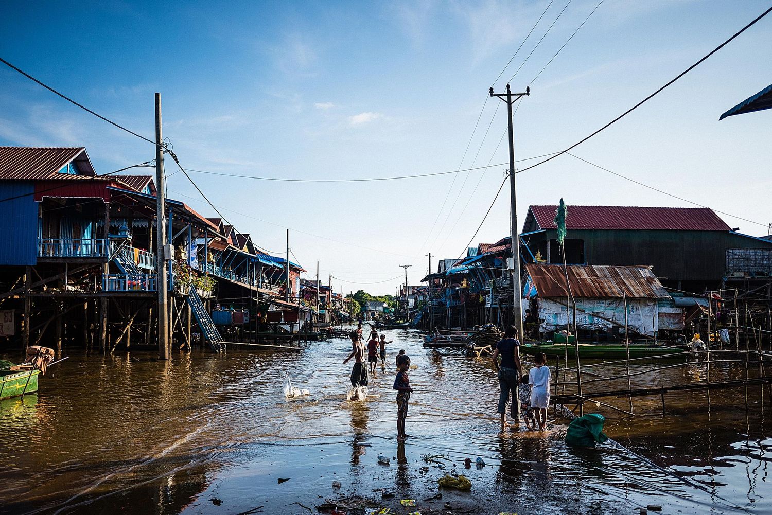 Flooded street with wooden houses on stilts and utility poles in a rural village during high water conditions.