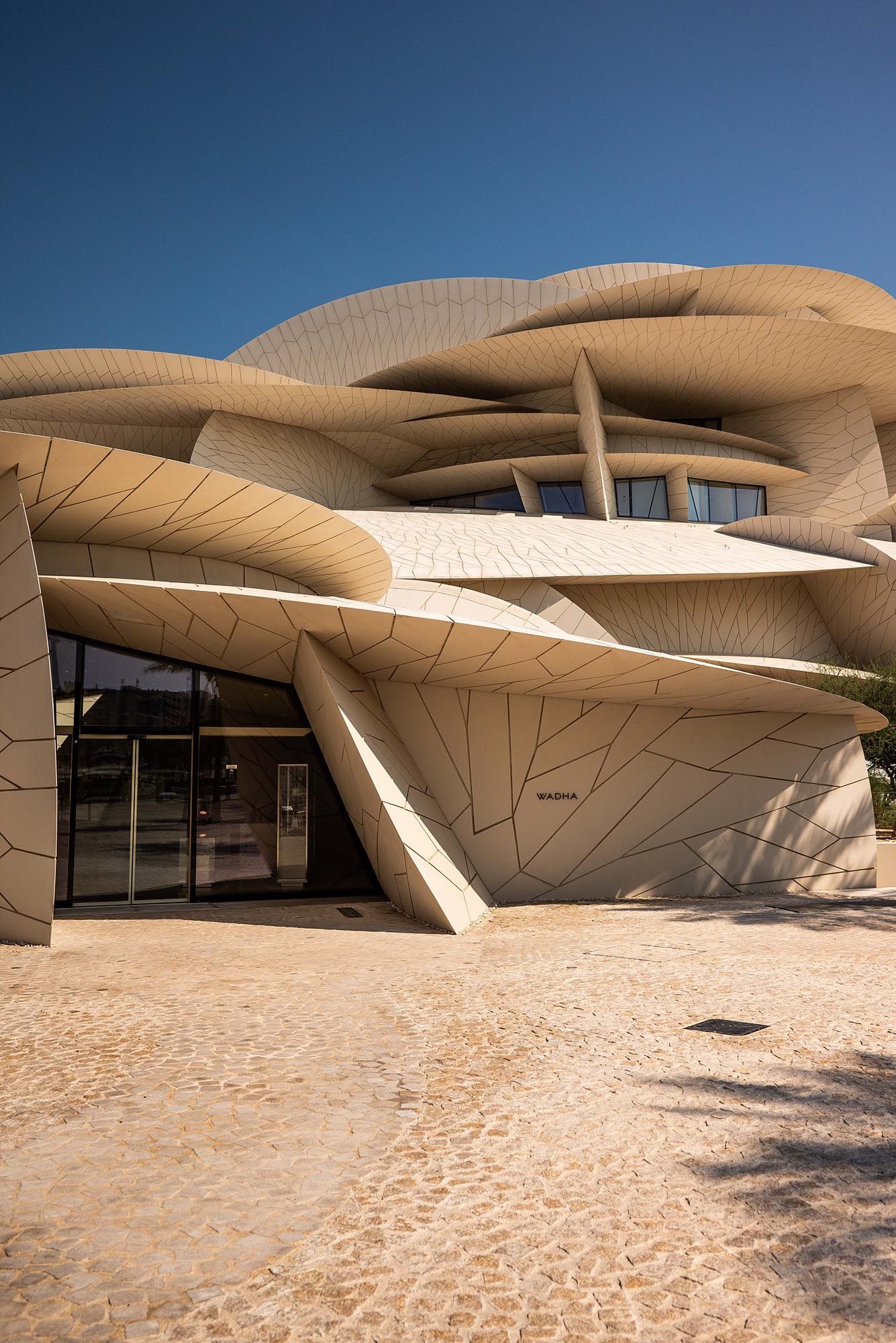 Modern desert museum building with curved sand-colored architecture and geometric patterns against blue sky in Qatar.