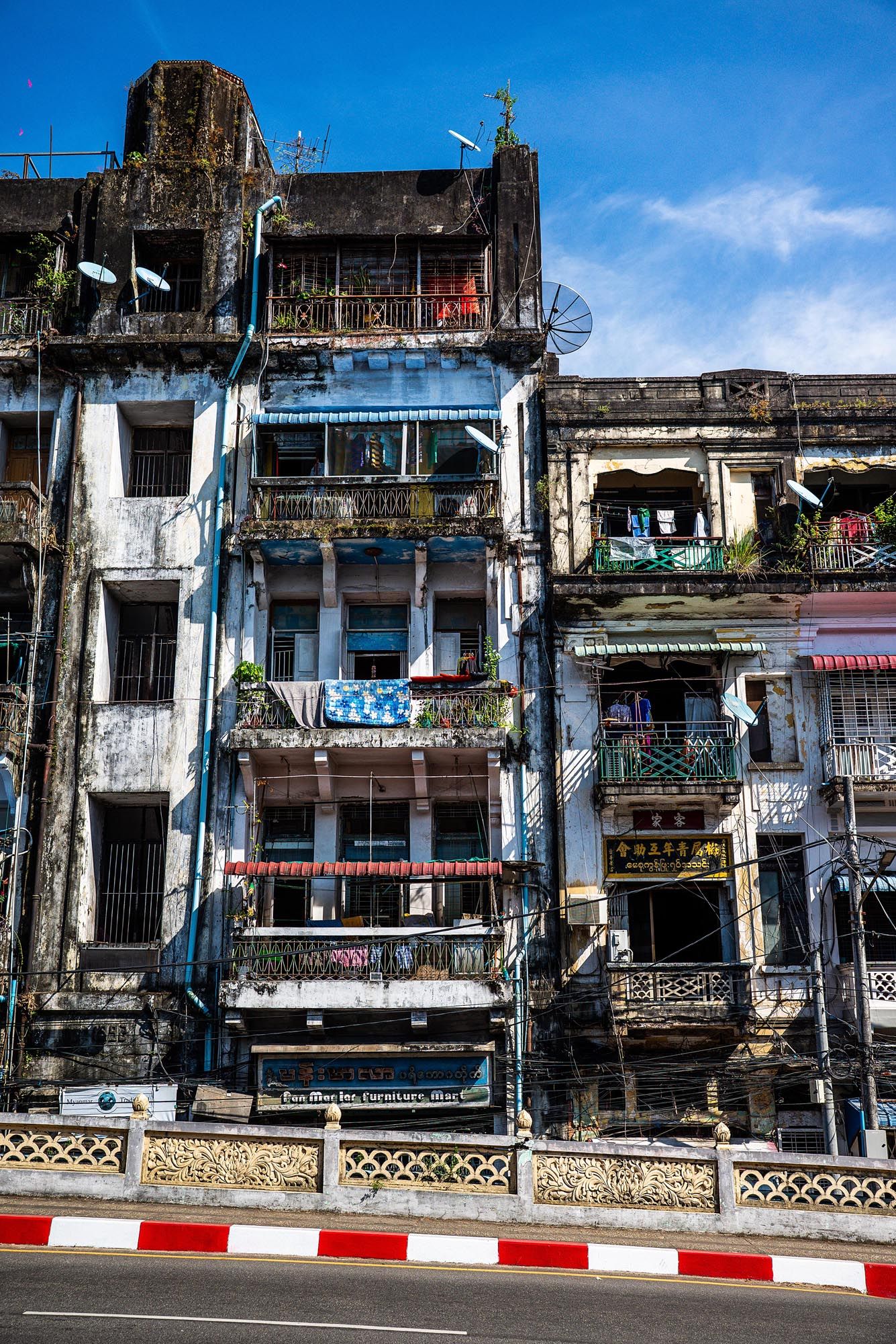 Row of weathered colonial-era buildings with balconies and peeling paint along a street in Southeast Asia.