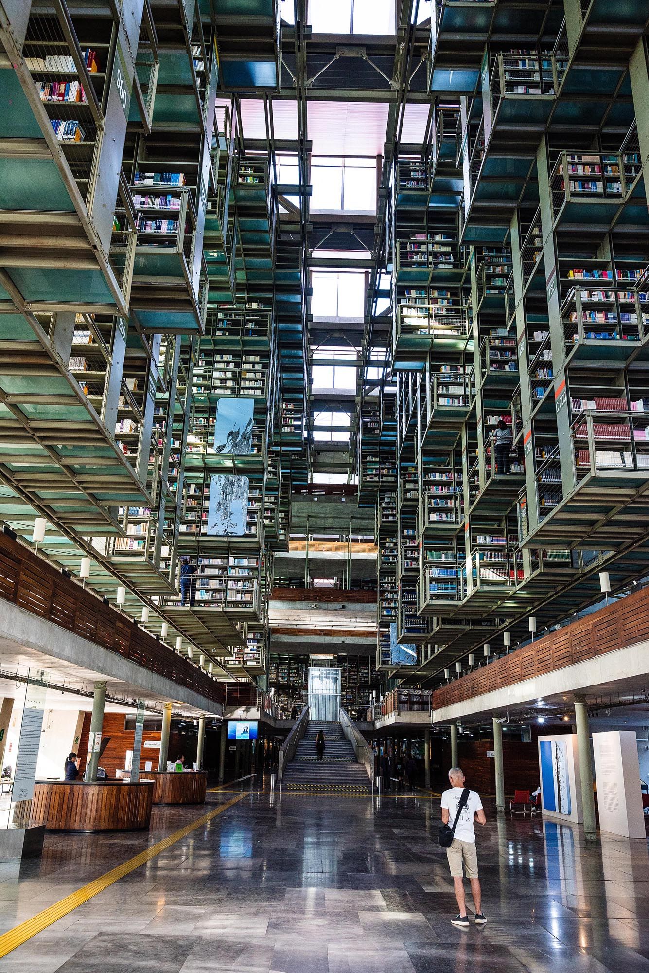 Modern library interior with towering multi-story bookshelves and skylights illuminating a polished marble floor.