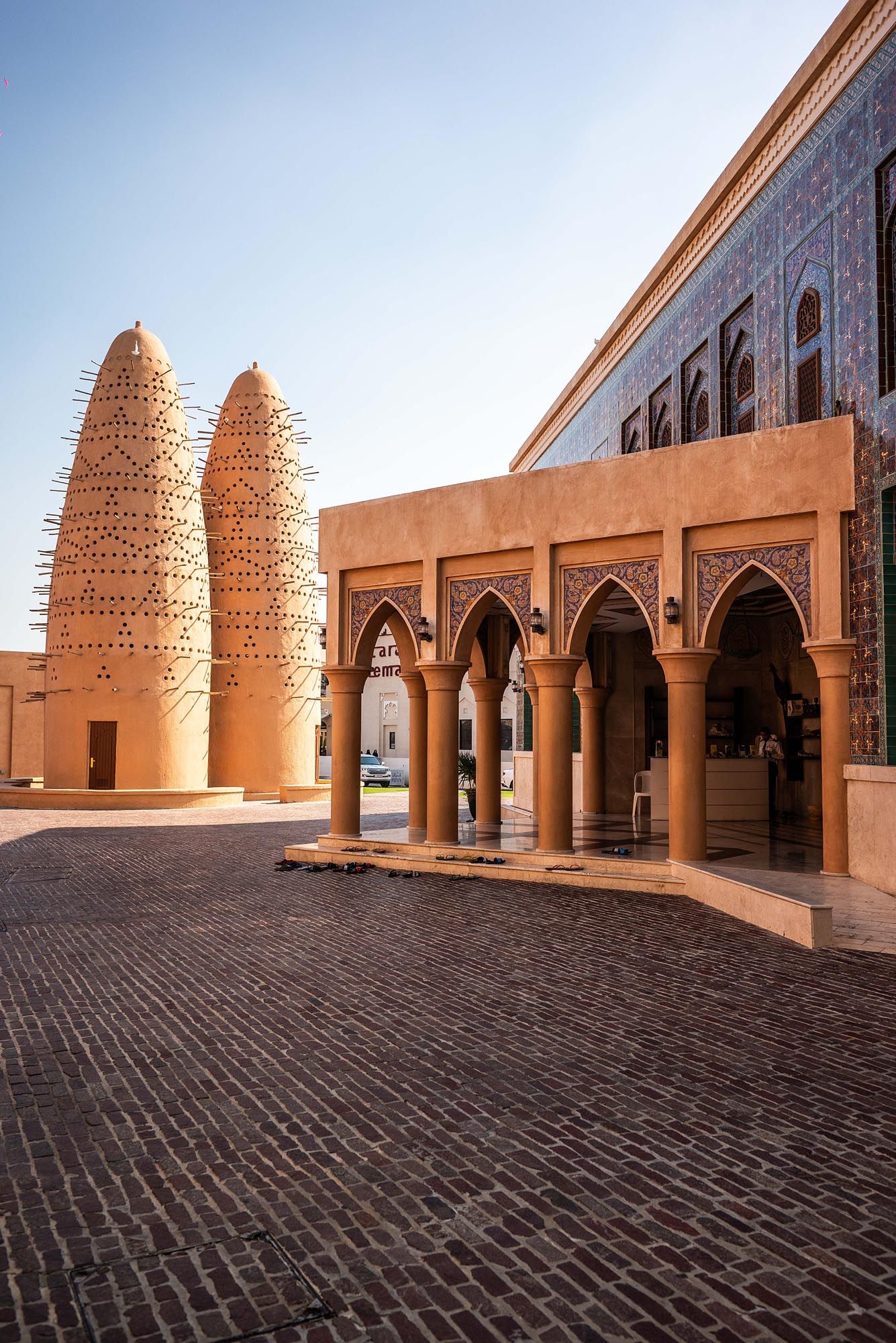Panoramic view of traditional Middle Eastern mosque architecture with arched walkways and decorative domed towers at sunset.