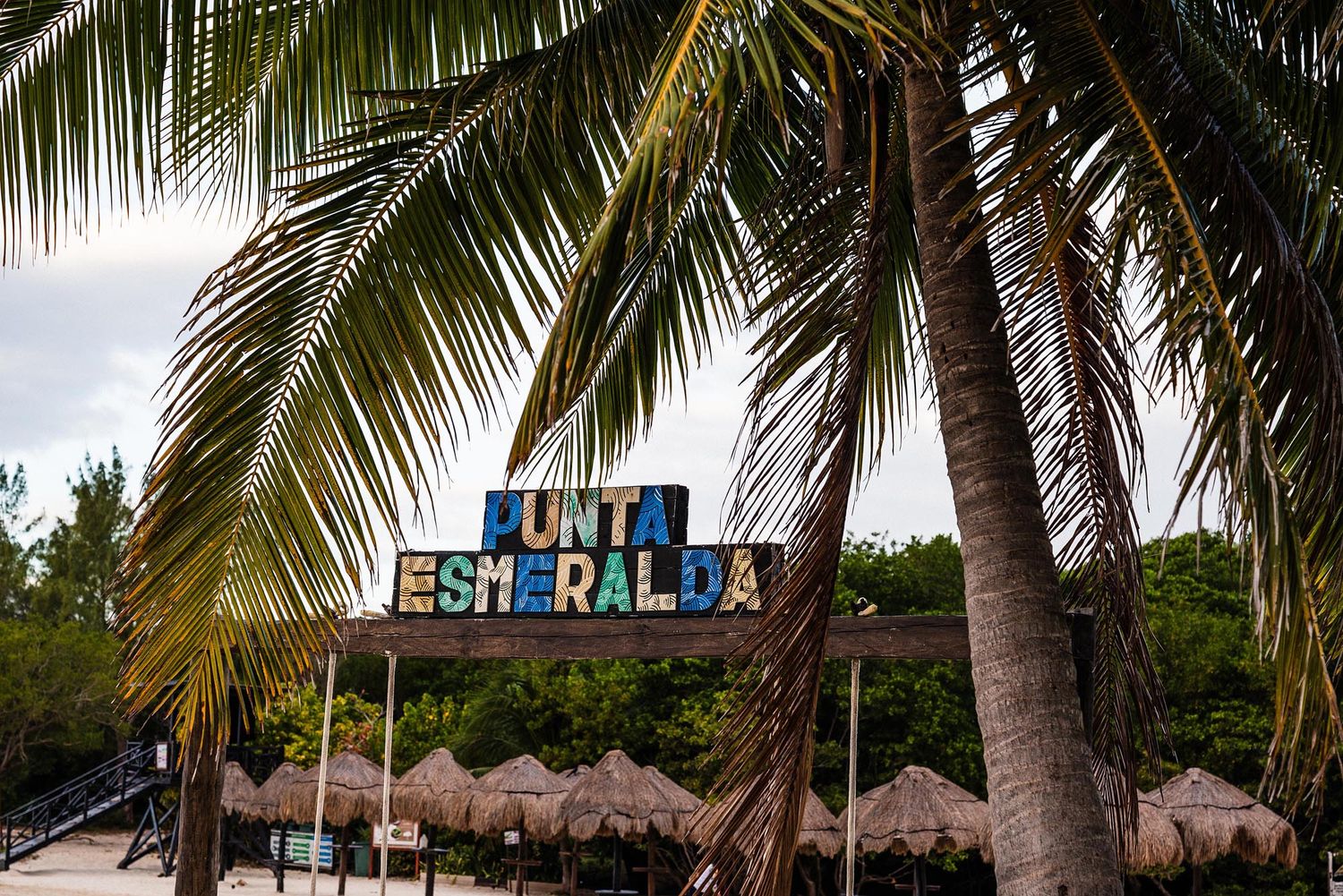 Palm trees and thatched-roof huts line a pristine tropical beach resort with crystal clear turquoise waters.