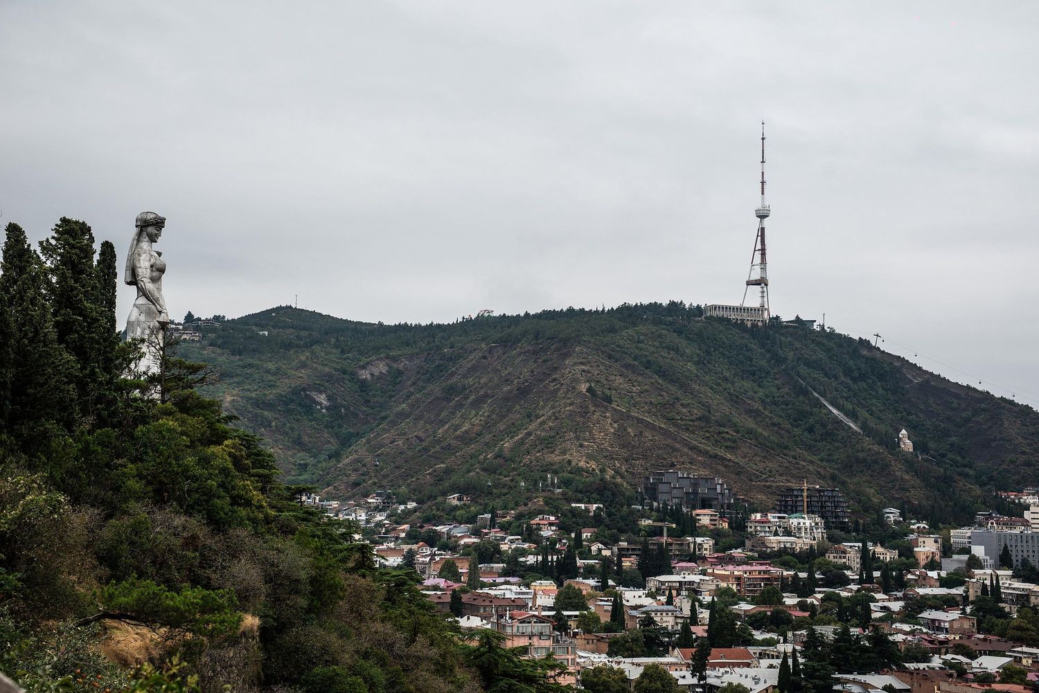 Hillside view of Tbilisi, Georgia with communication tower on mountain peak and residential buildings below.