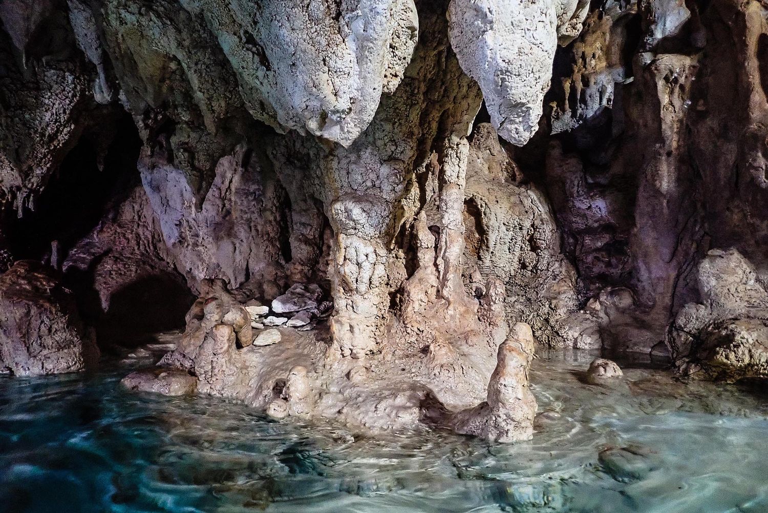 Stunning underground cave system with crystal clear turquoise water reflecting off limestone formations and rocky walls.