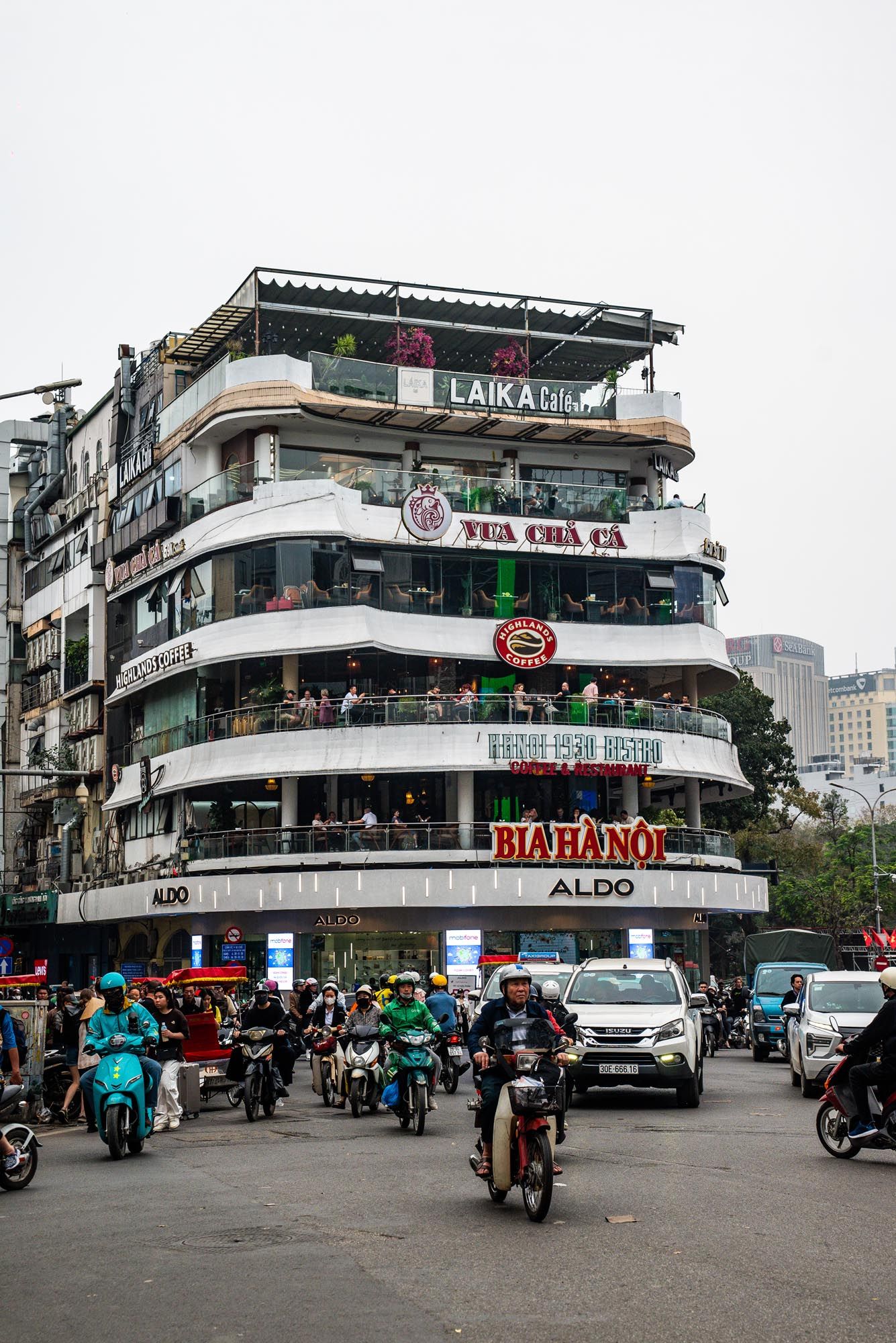 Panoramic view of a busy street corner in Vietnam with scooters and storefronts featuring retail shops and restaurants.