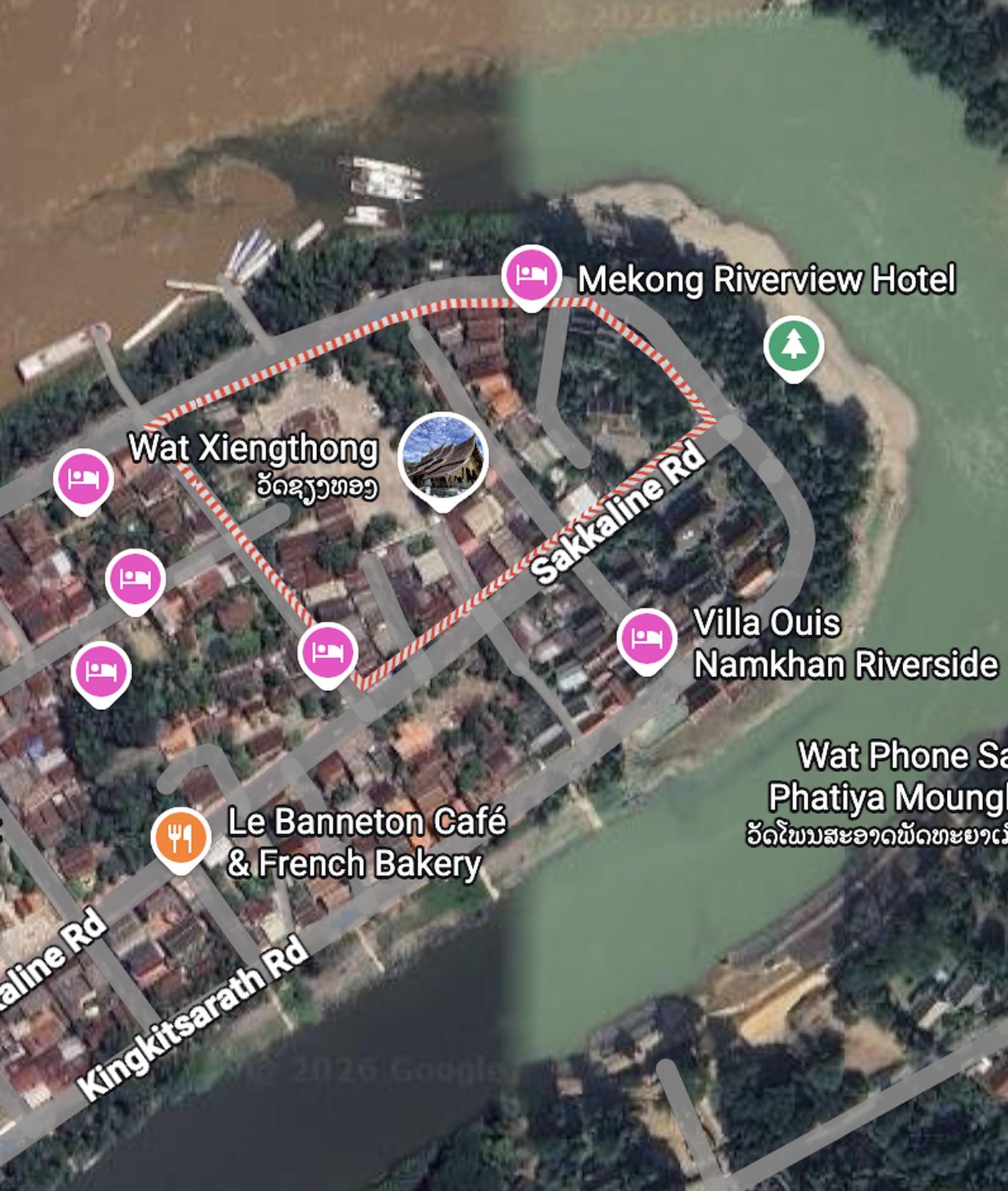 Aerial view of a riverside town with buildings and roads along a curved waterfront showing pink location markers.