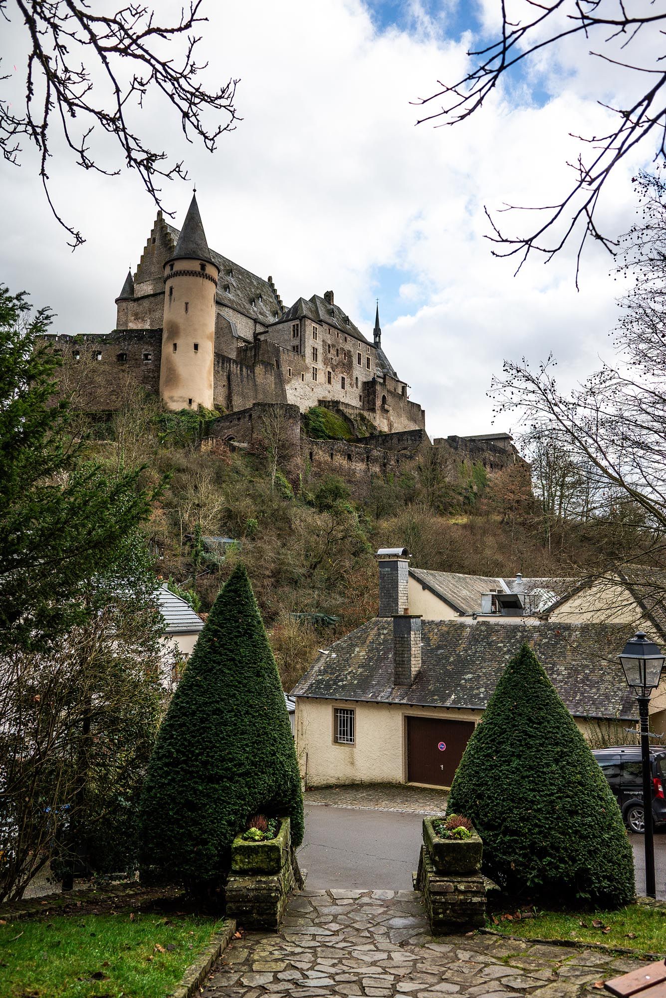 Medieval castle perched on a hilltop with manicured topiary gardens and stone pathways leading to the entrance.
