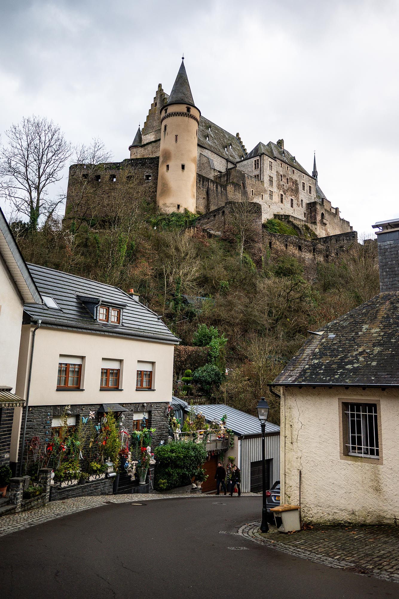 Medieval Vianden Castle perched on a hilltop in Luxembourg with white buildings nestled along the winding road below.