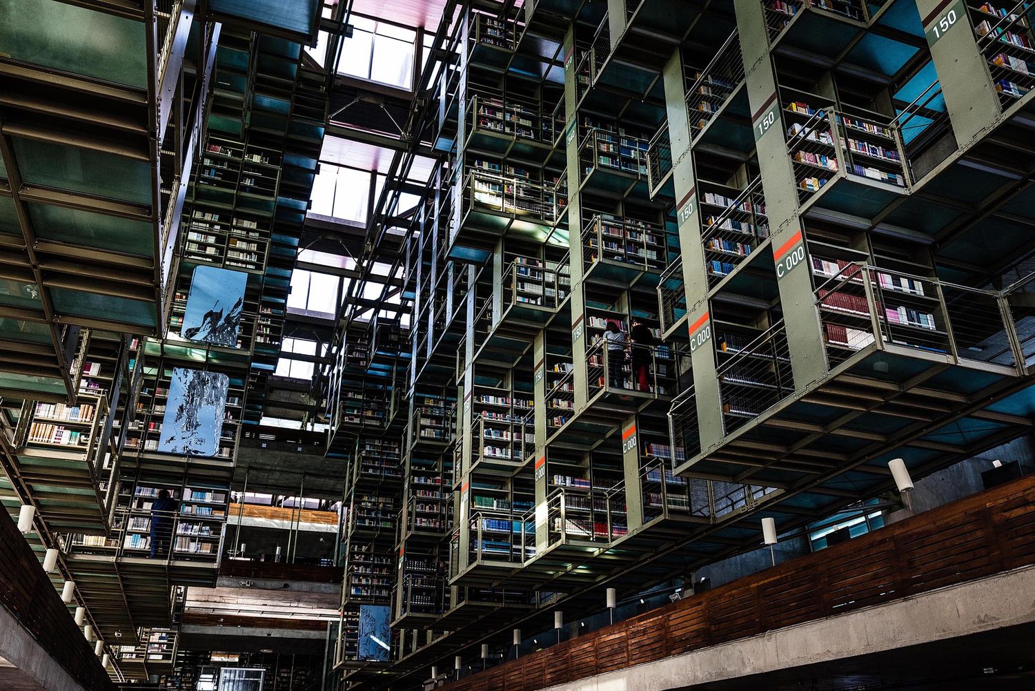 Interior view of a large multi-level library with metal shelving and rows of books extending into the distance.