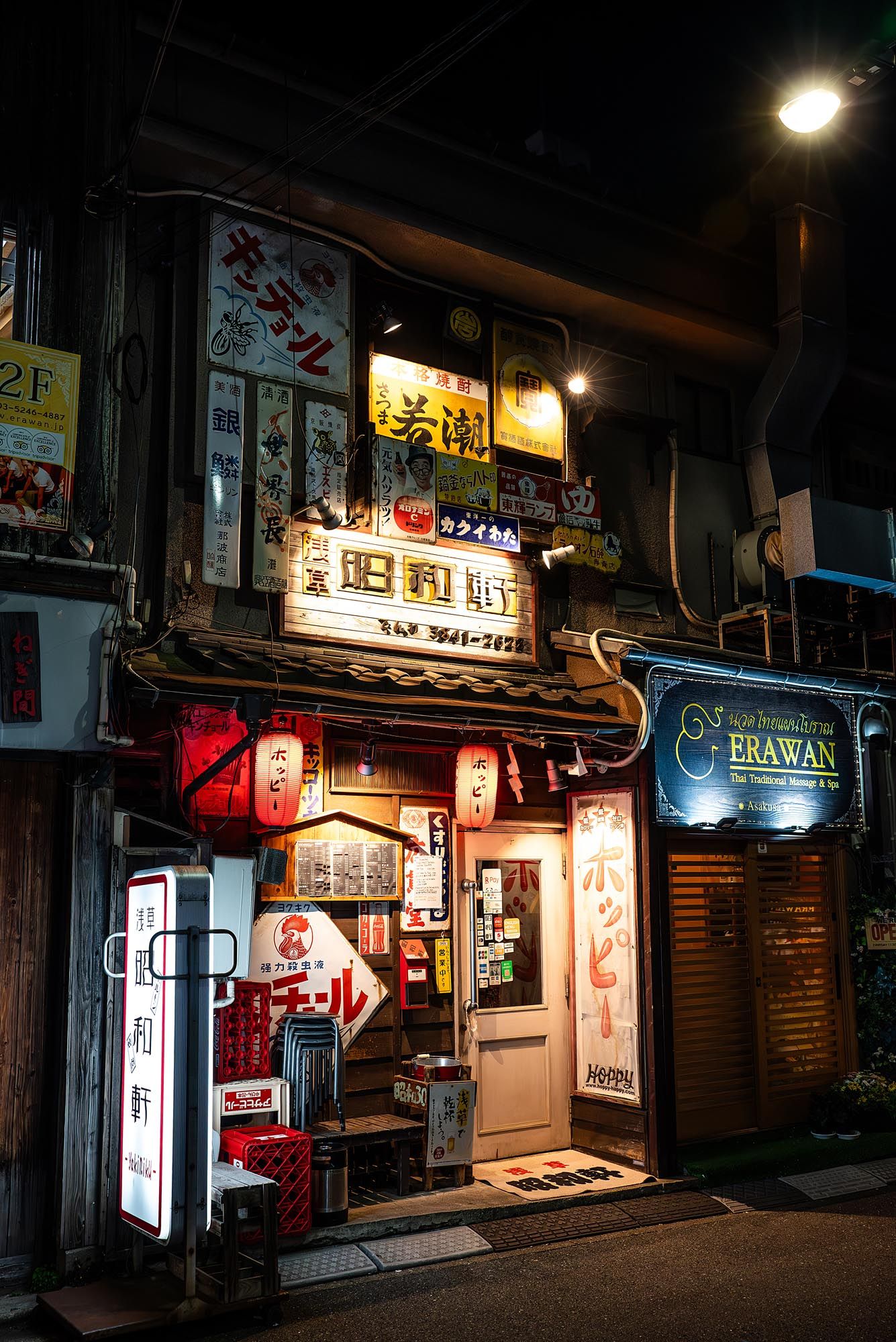 Dimly lit Japanese street at night with illuminated storefront signs and closed shop shutters in an urban alleyway.