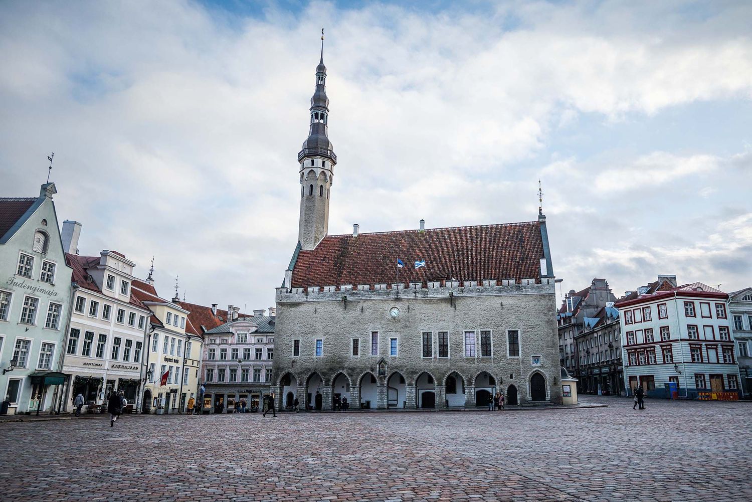Historic buildings and medieval architecture line the town square of Tallinn, Estonia under cloudy skies.