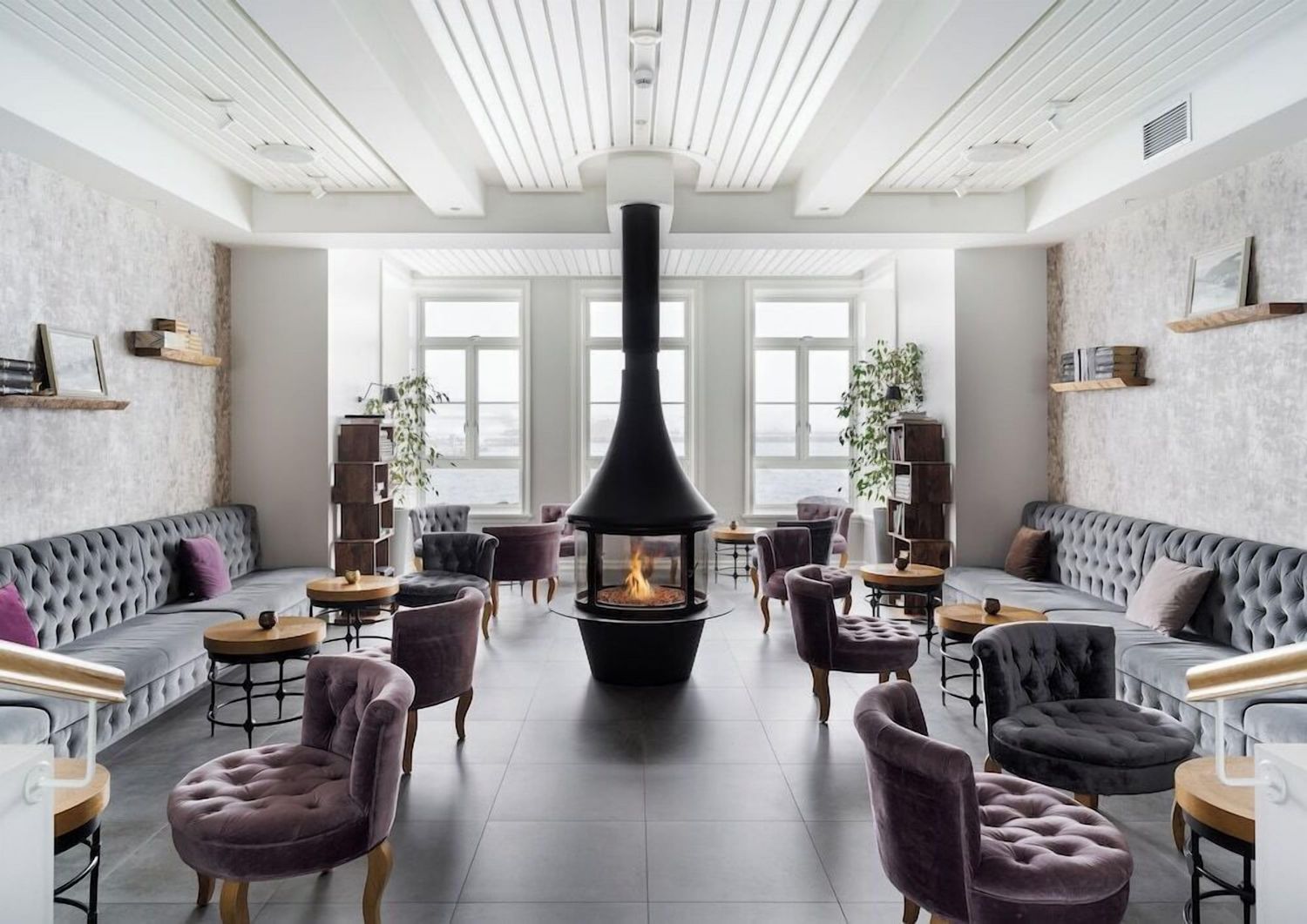 Modern Scandinavian living room features tufted gray sofa, suspended fireplace, and white walls with natural lighting.