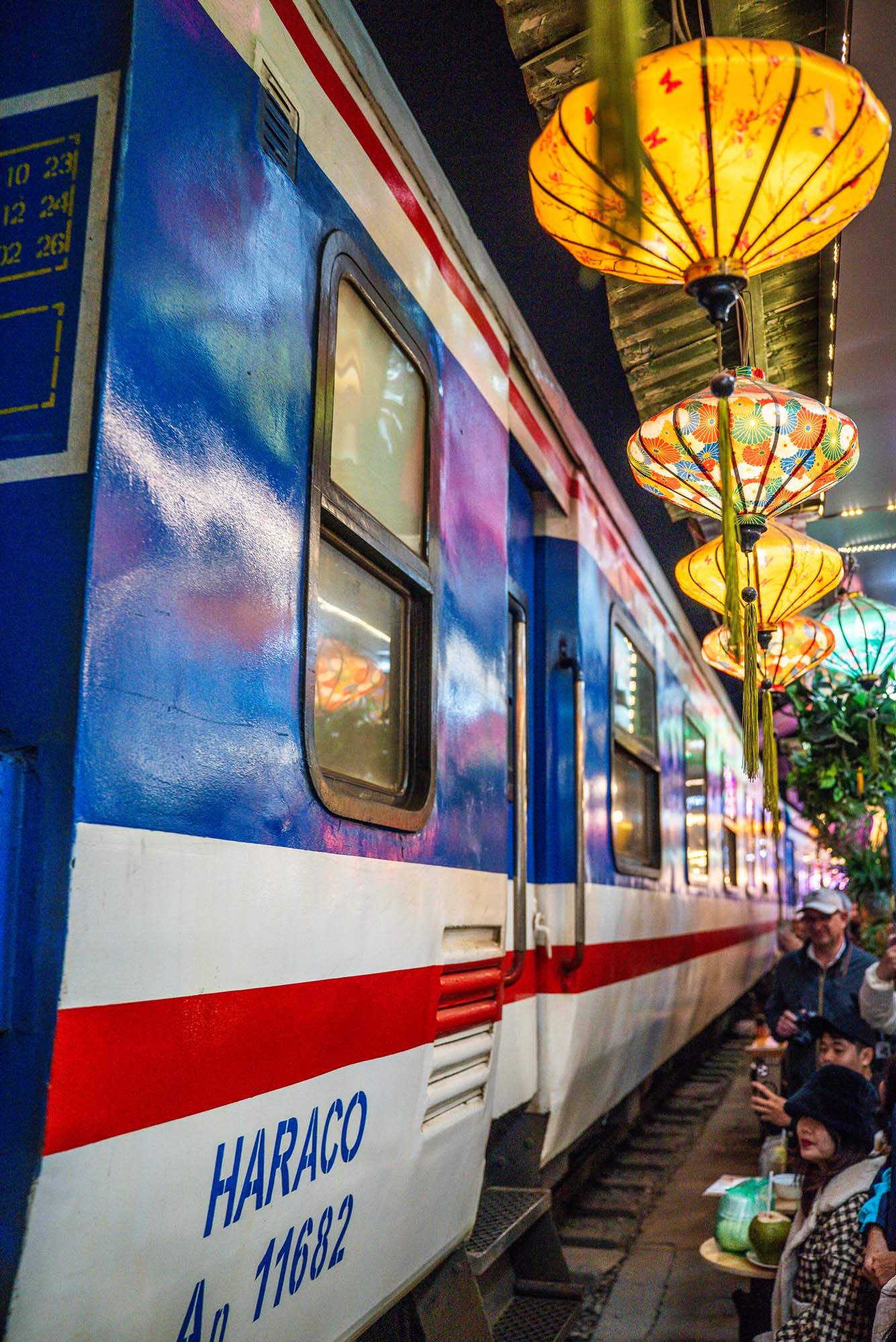 Train car interior decorated with warm glowing yellow lanterns and traditional Chinese design elements along blue walls.