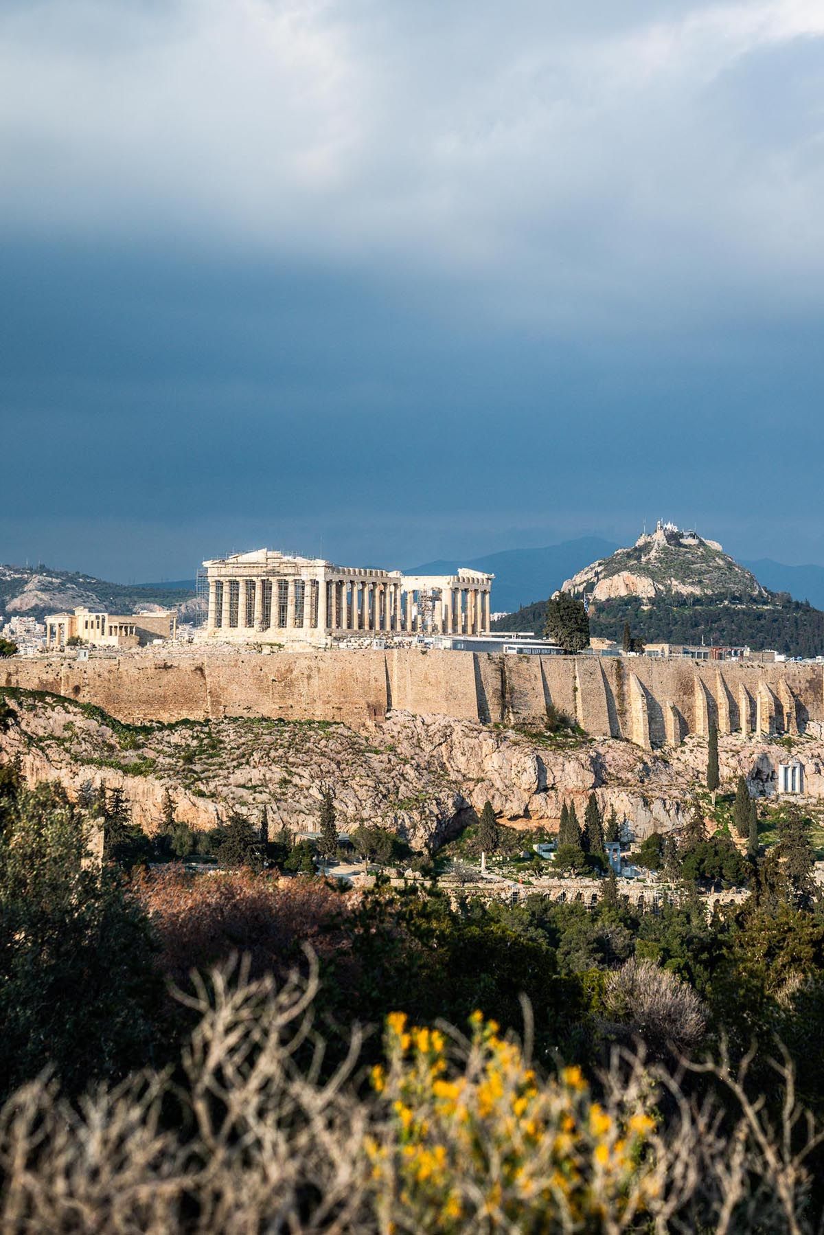 Panoramic view of the ancient Acropolis of Athens with Parthenon temple atop rocky hill against cloudy sky.