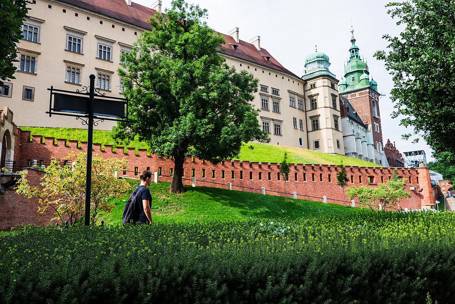 Historic Wawel Castle and Cathedral towers rise above lush green gardens and walking paths in Krakow, Poland.