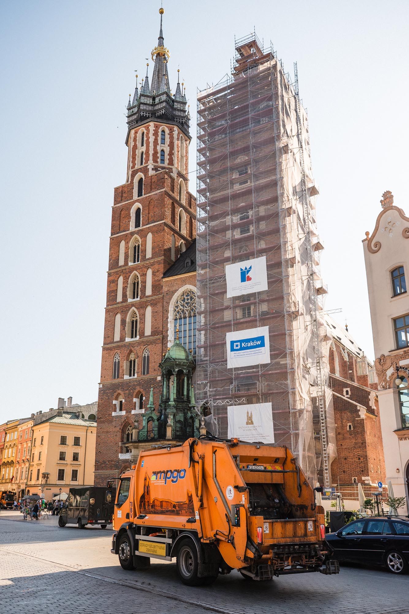 Orange garbage truck collecting waste in front of St. Mary's Basilica historic church towers in Krakow, Poland.