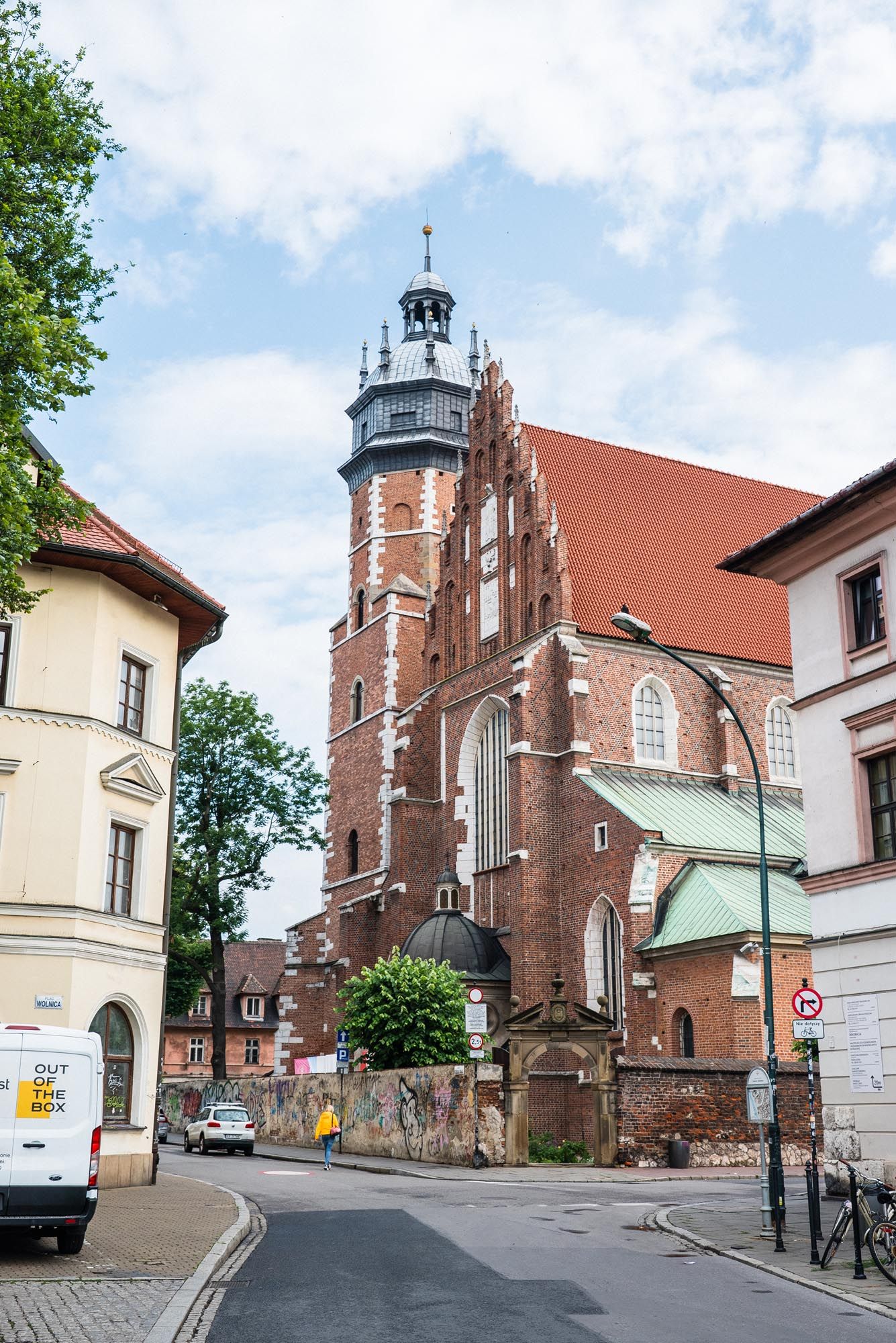Historic red brick church with tall tower and Gothic architecture on a street corner in Krakow, Poland.
