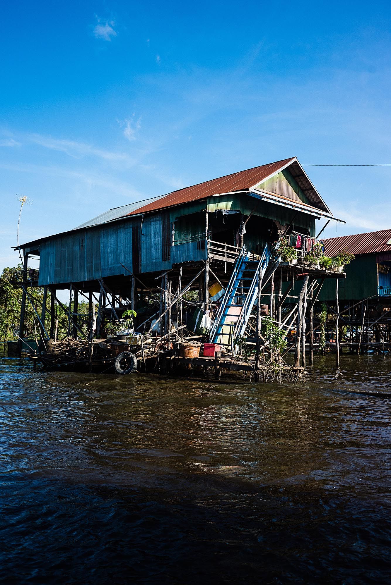 Traditional wooden stilt house on the water with blue exterior and rustic red roof in Southeast Asia.