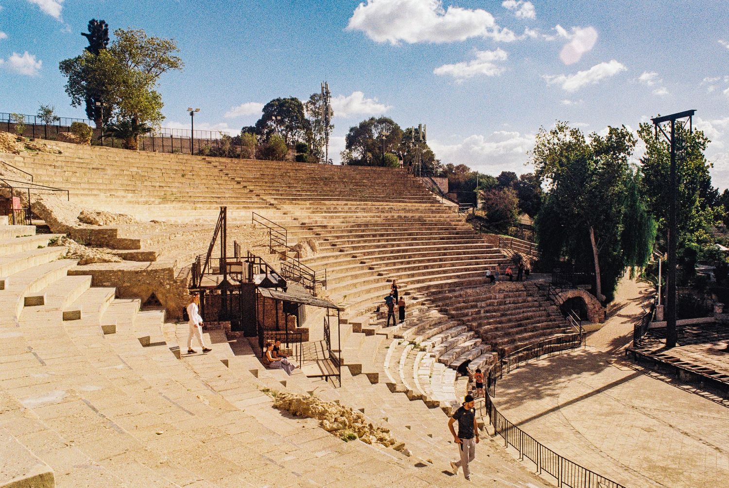 Ancient stone amphitheater ruins with curved rows of seats under blue sky at archaeological site in sunny weather.