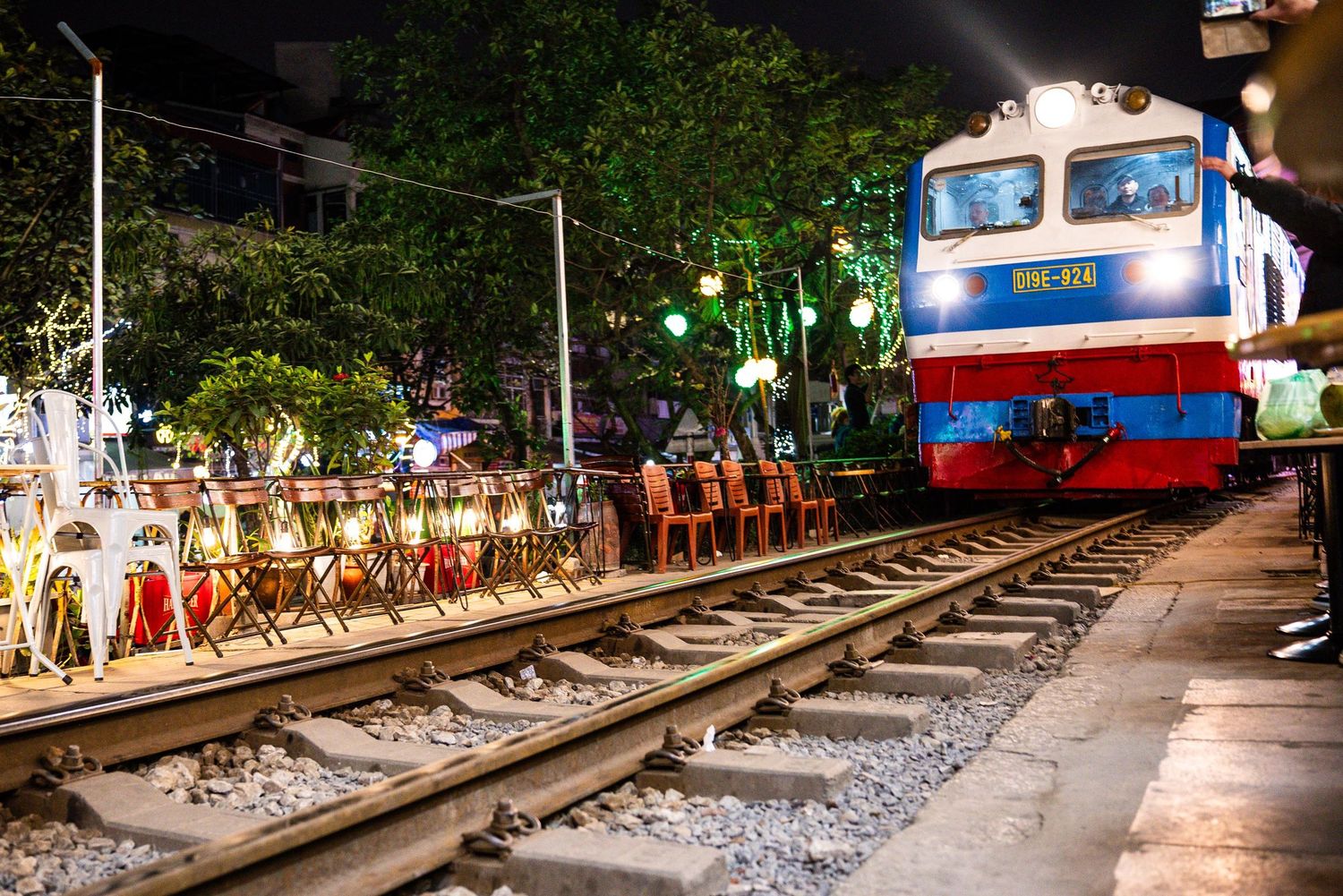 A train passing through a vibrant street market in Hanoi with stalls and cafes lining the narrow railway tracks.