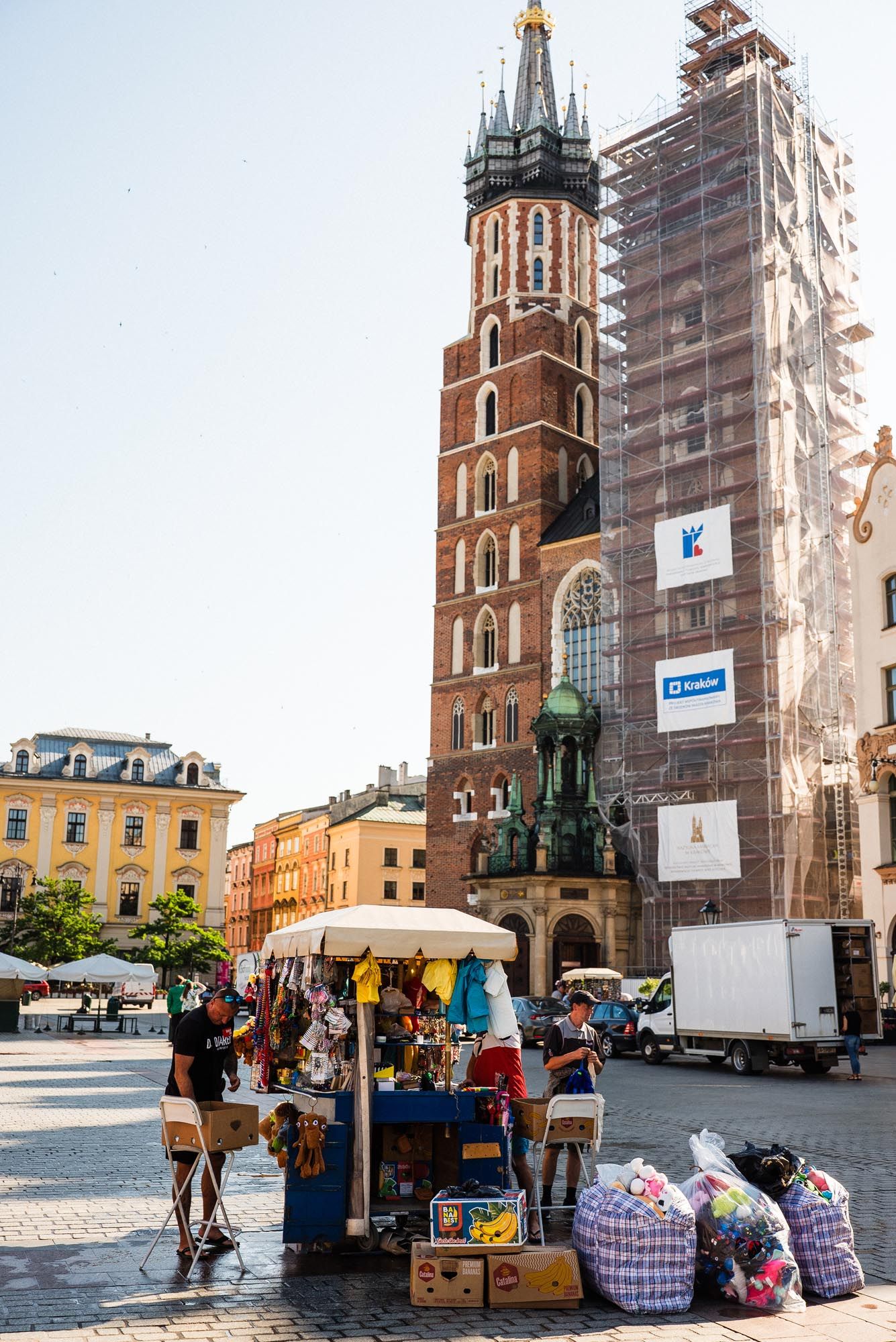 Street vendor stall beneath historic St. Mary's Basilica tower with scaffolding in Krakow's Main Market Square.
