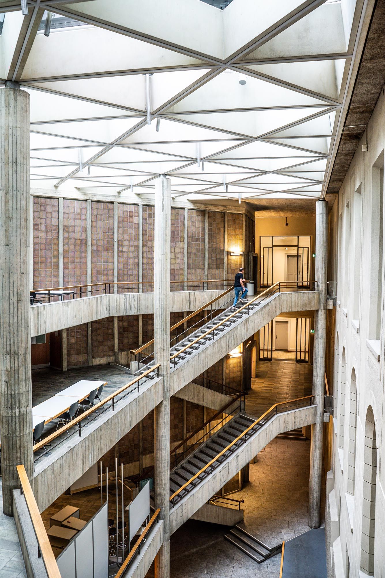 Panoramic view of a modern industrial interior with concrete columns, metal staircases and angular walkways under skylights.