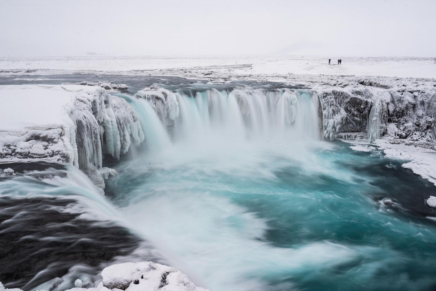 Majestic Godafoss waterfall cascades over icy cliffs in winter, creating turquoise pools in northern Iceland.