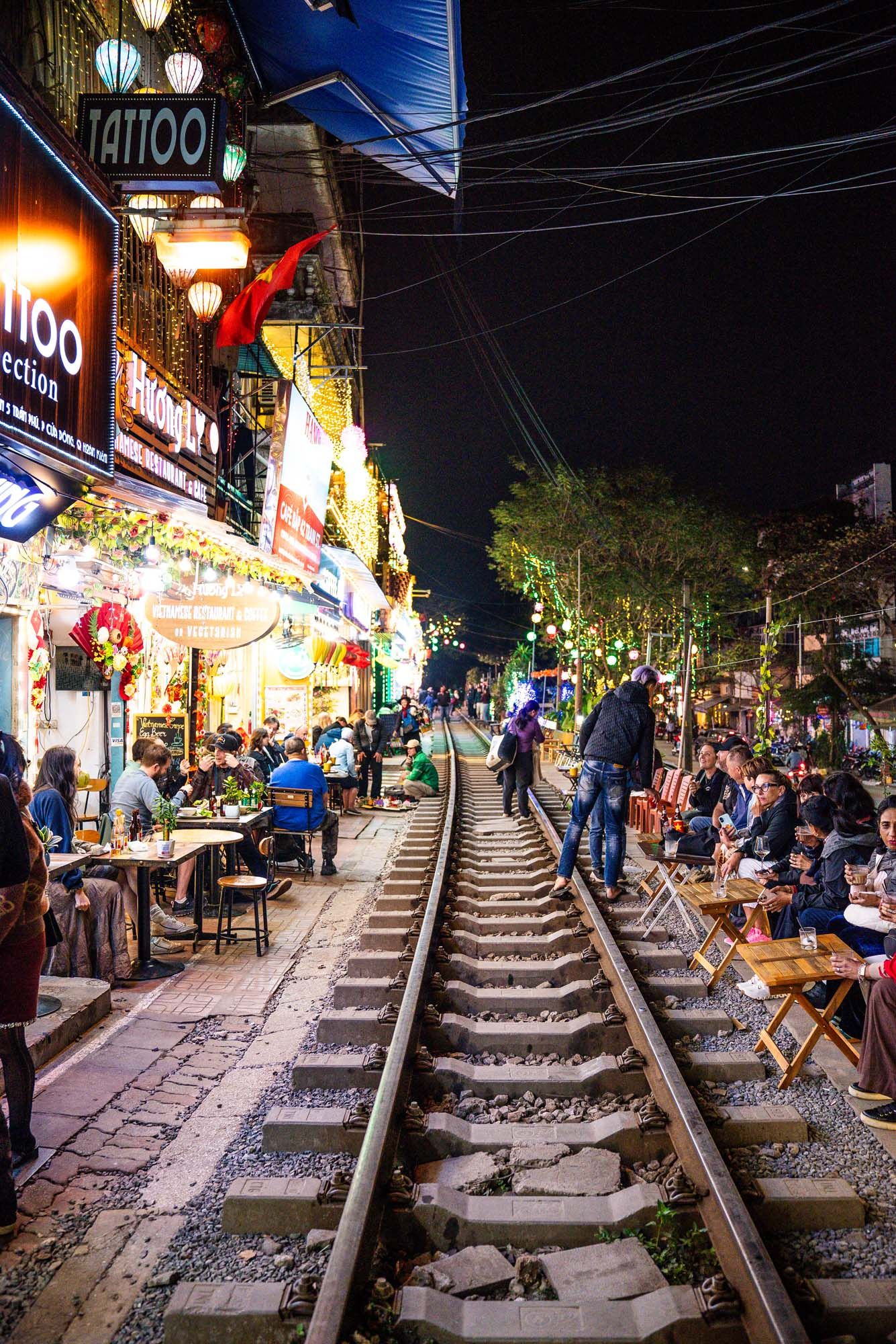 Night view of illuminated shops and restaurants along old train tracks in Hanoi's Train Street, Vietnam.