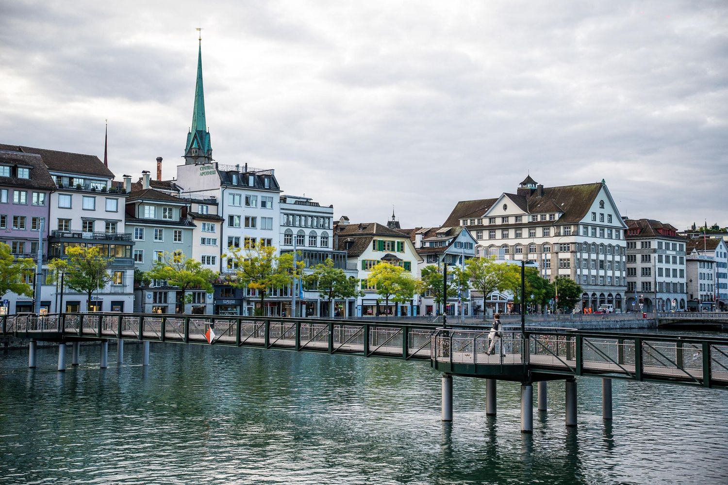 Panoramic view of a traditional Swiss lakeside town with historic buildings and church spires reflected in calm waters.