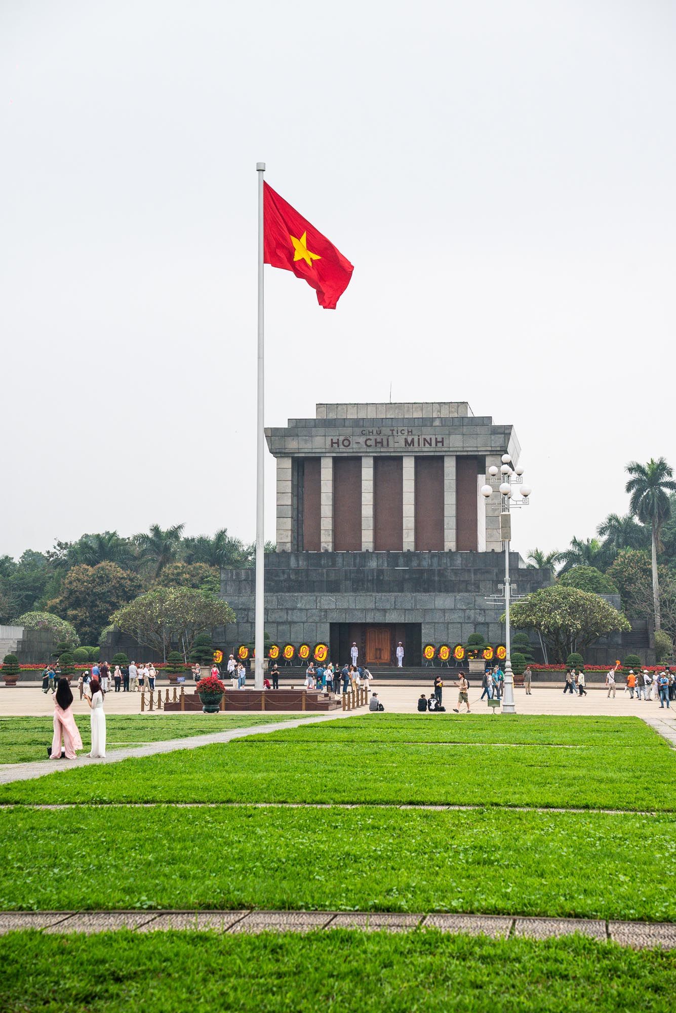 Ho Chi Minh Mausoleum in Hanoi, Vietnam with red flag flying and green lawn in the foreground.
