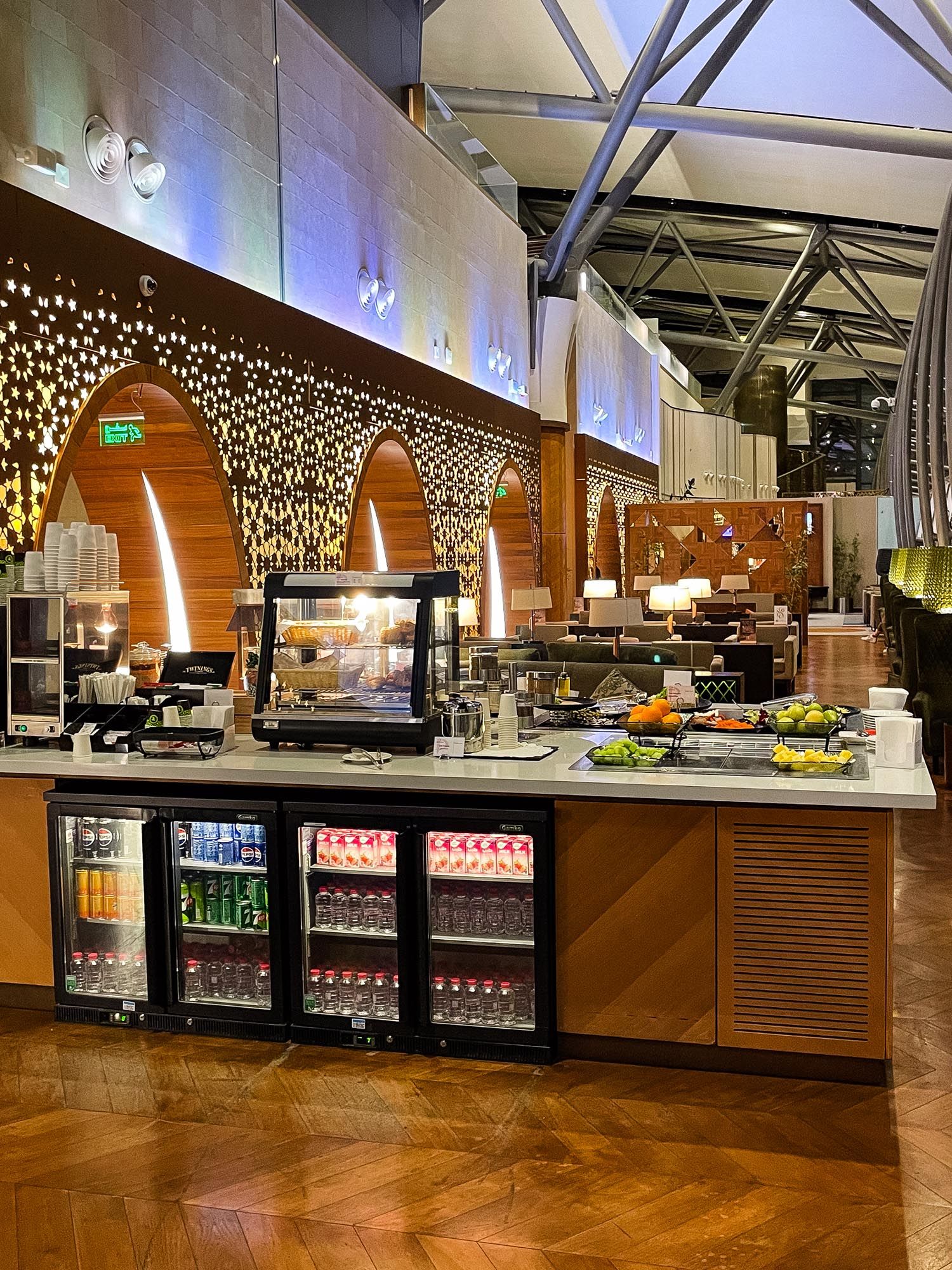 Modern cafeteria serving area with wood paneling, glass display cases, and decorative pendant lighting along the counter.