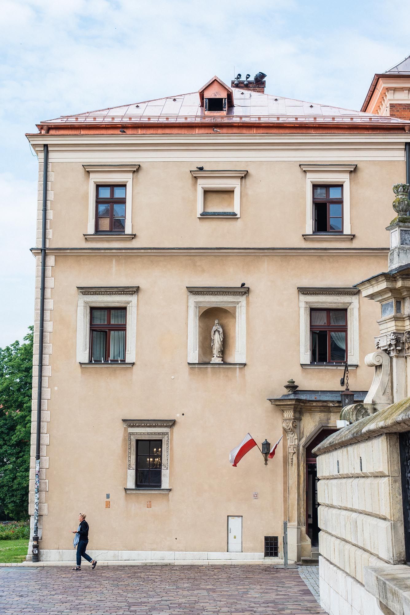 Historic beige building facade with windows, a religious statue niche, and Polish flag on Wawel Castle grounds in Krakow.